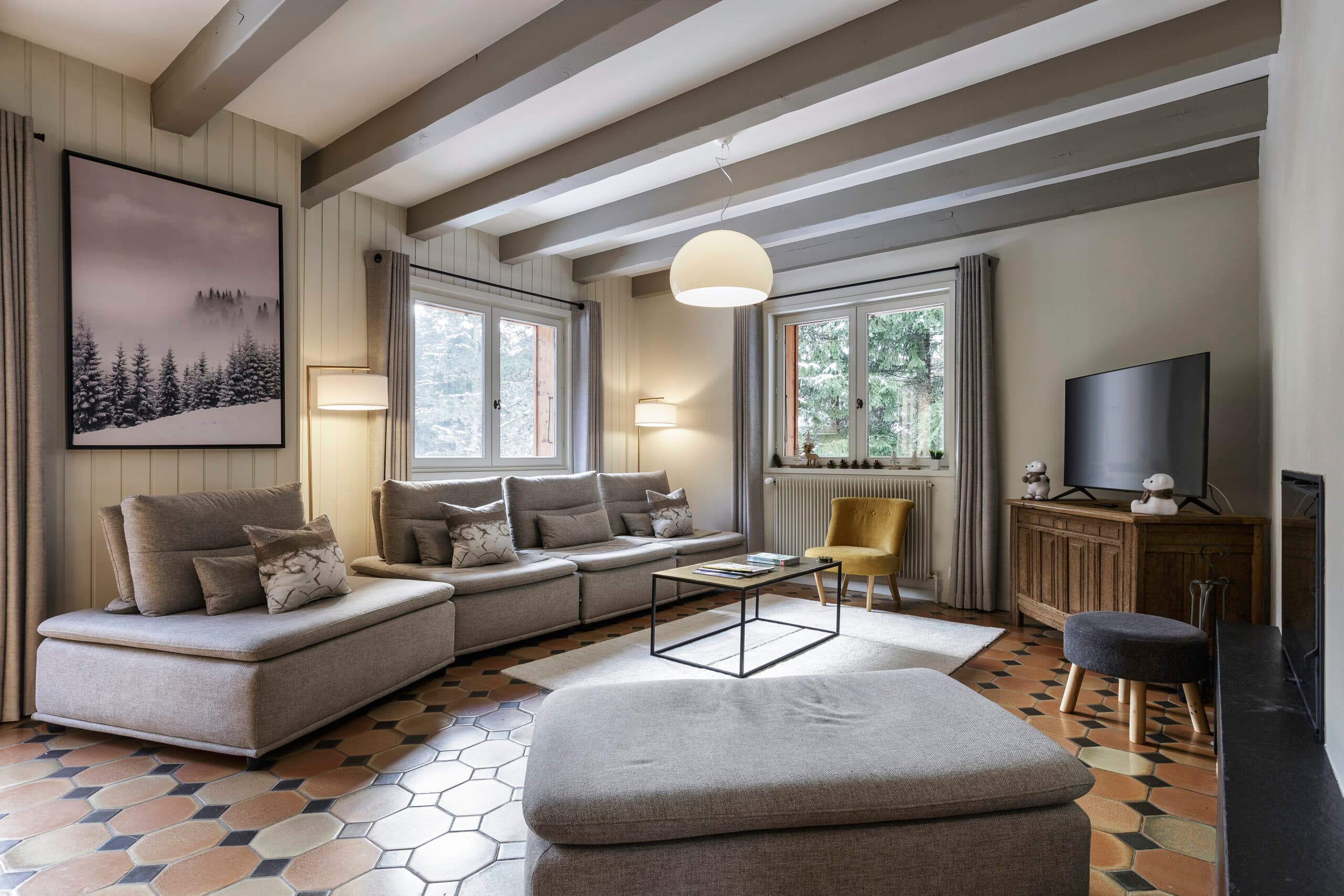 A bright and spacious living room, with a grey sofa, puff and a coffee table in the center.