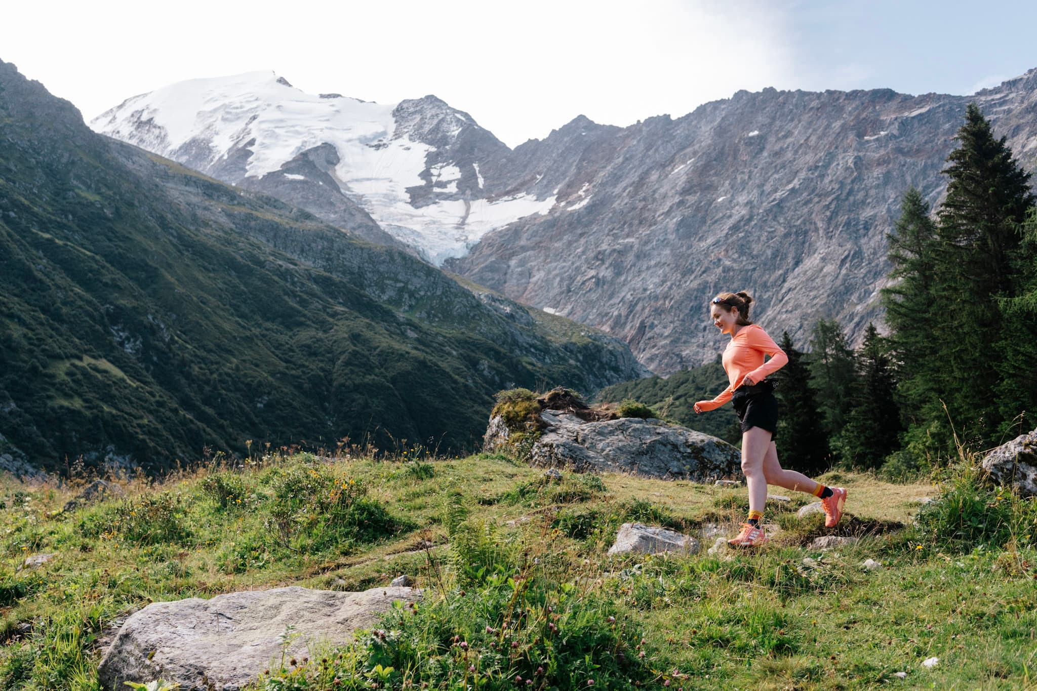 1 runner runs down hill in alpine meadow with alpine mountains above