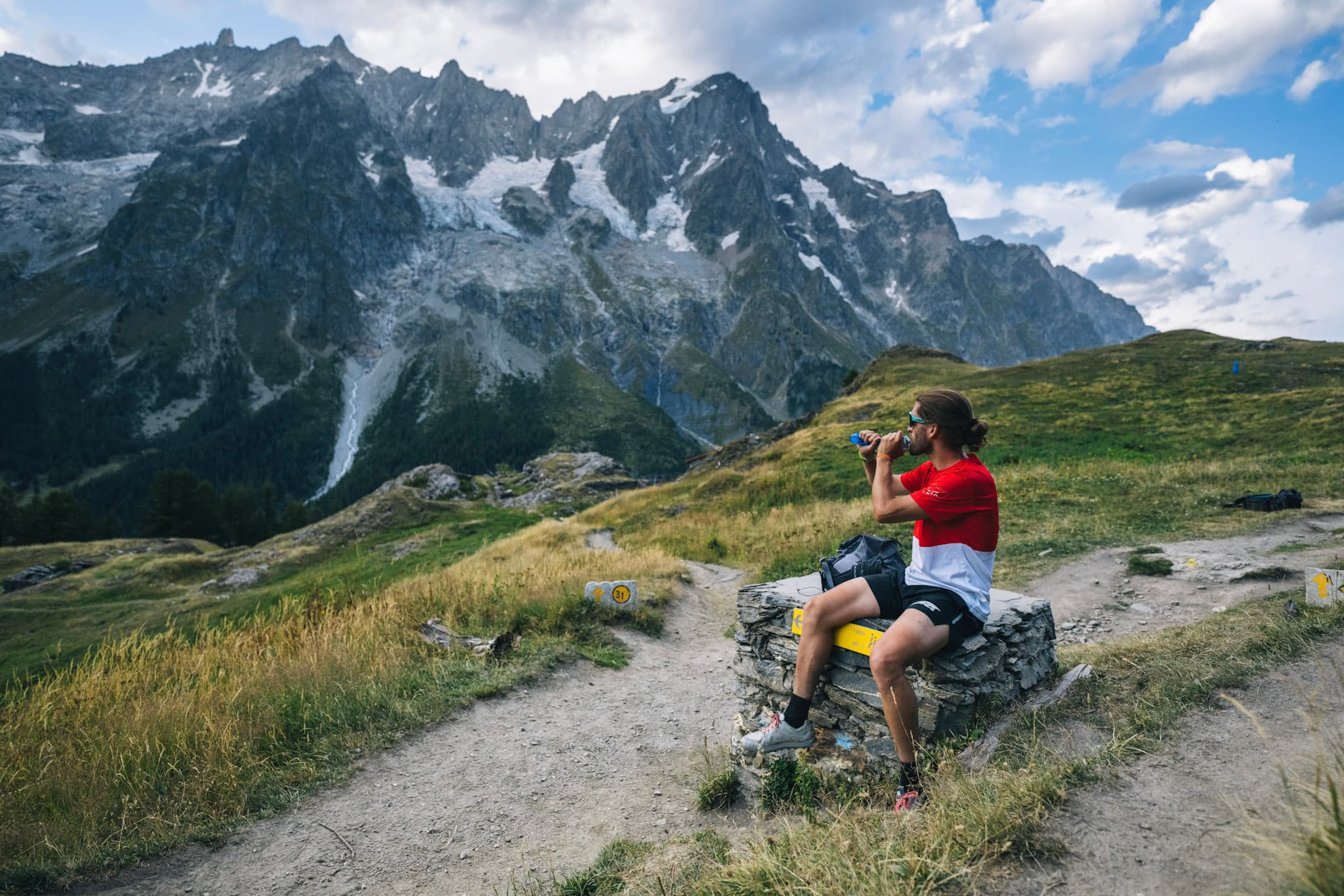 runner sits and takes a drink while looking at alpine mountains