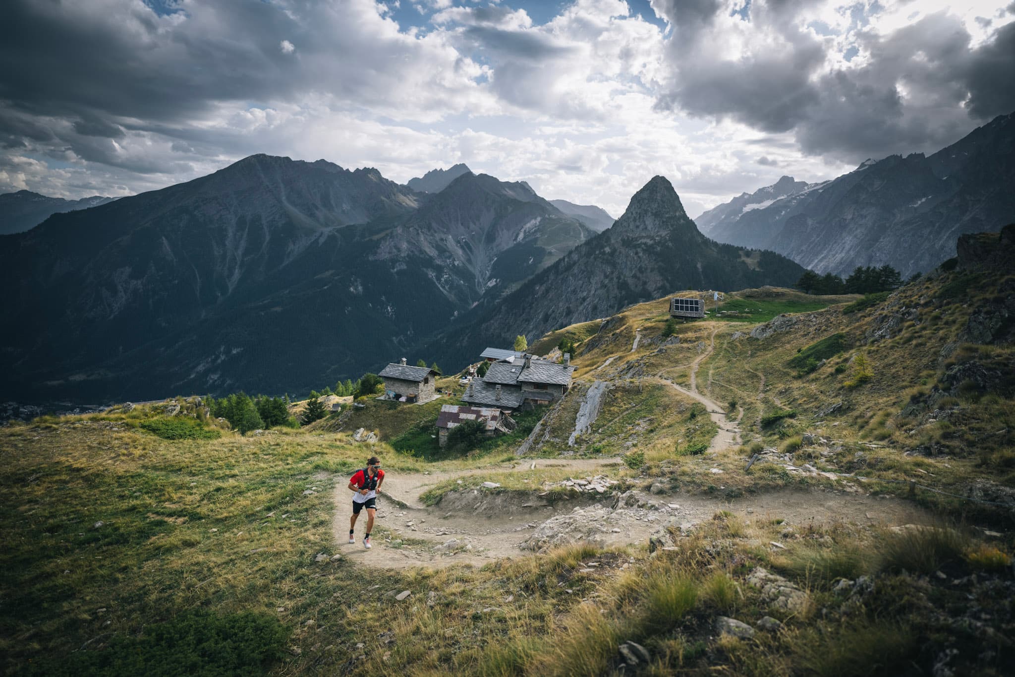 runner running up hill with mountains and mountain refuge in background