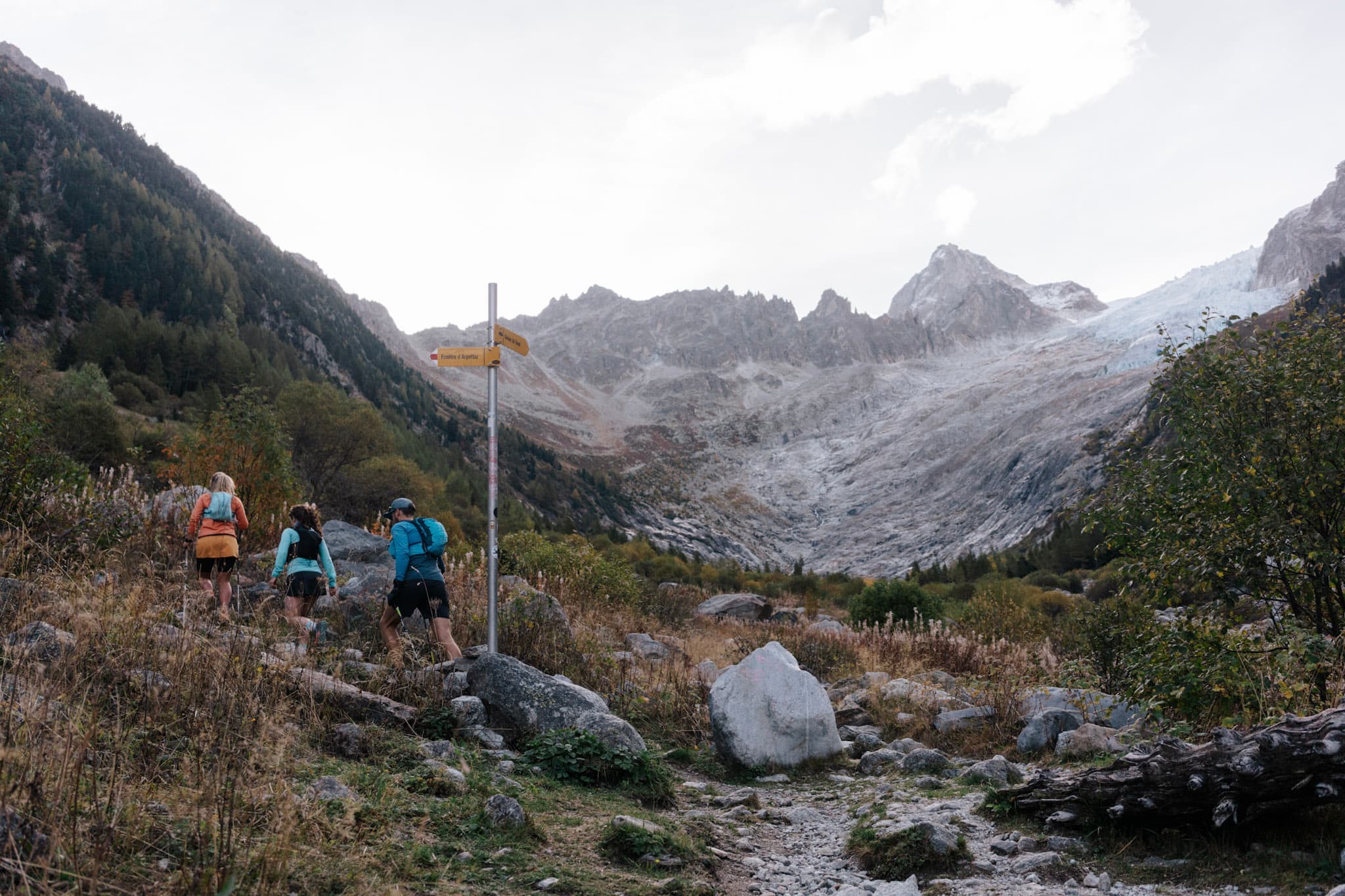 3 runners hike up hill early morning with Alpine mountains above