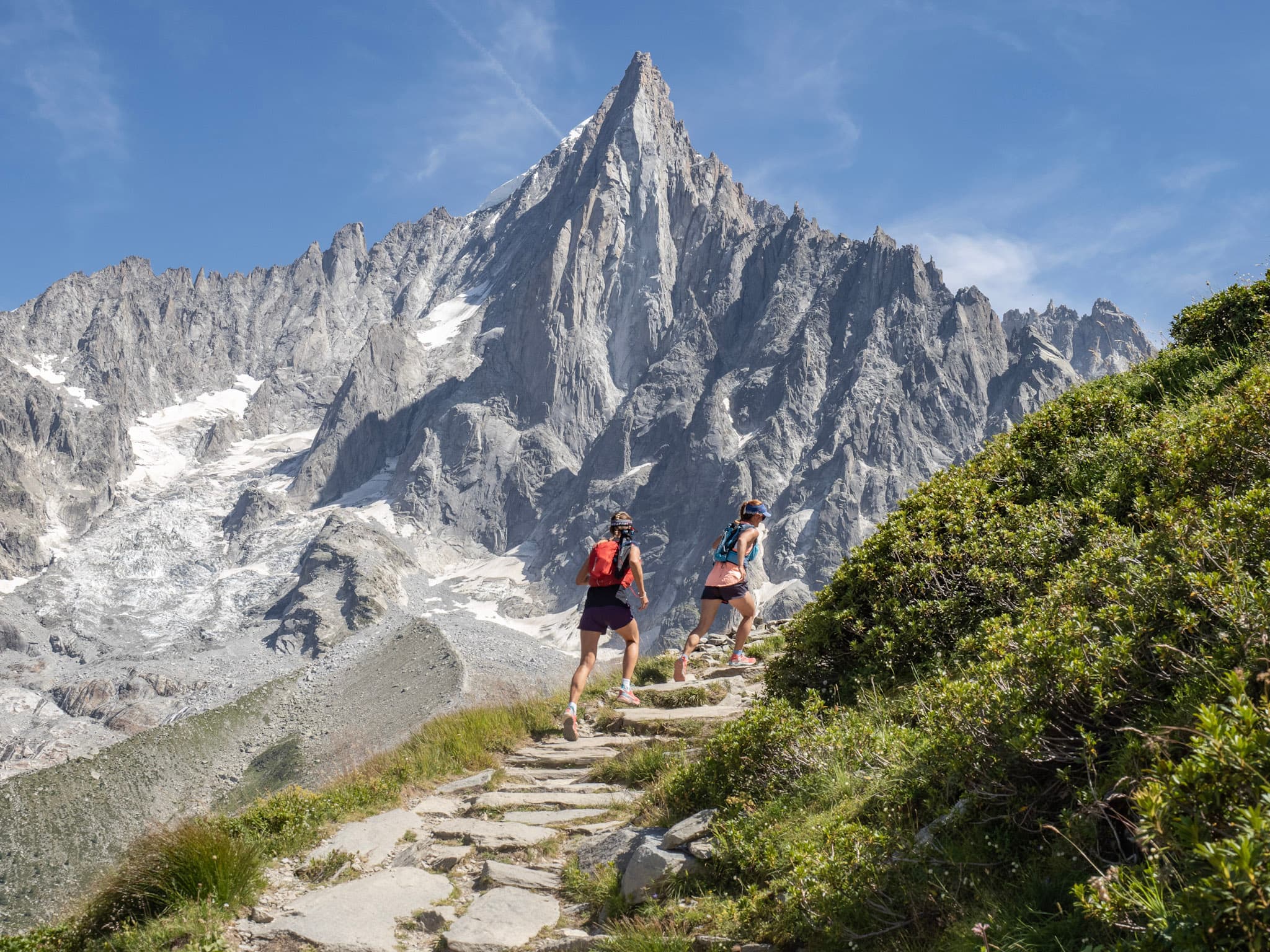 to runners run uphill on Rocky Trail with pointy Rocky Mountain behind