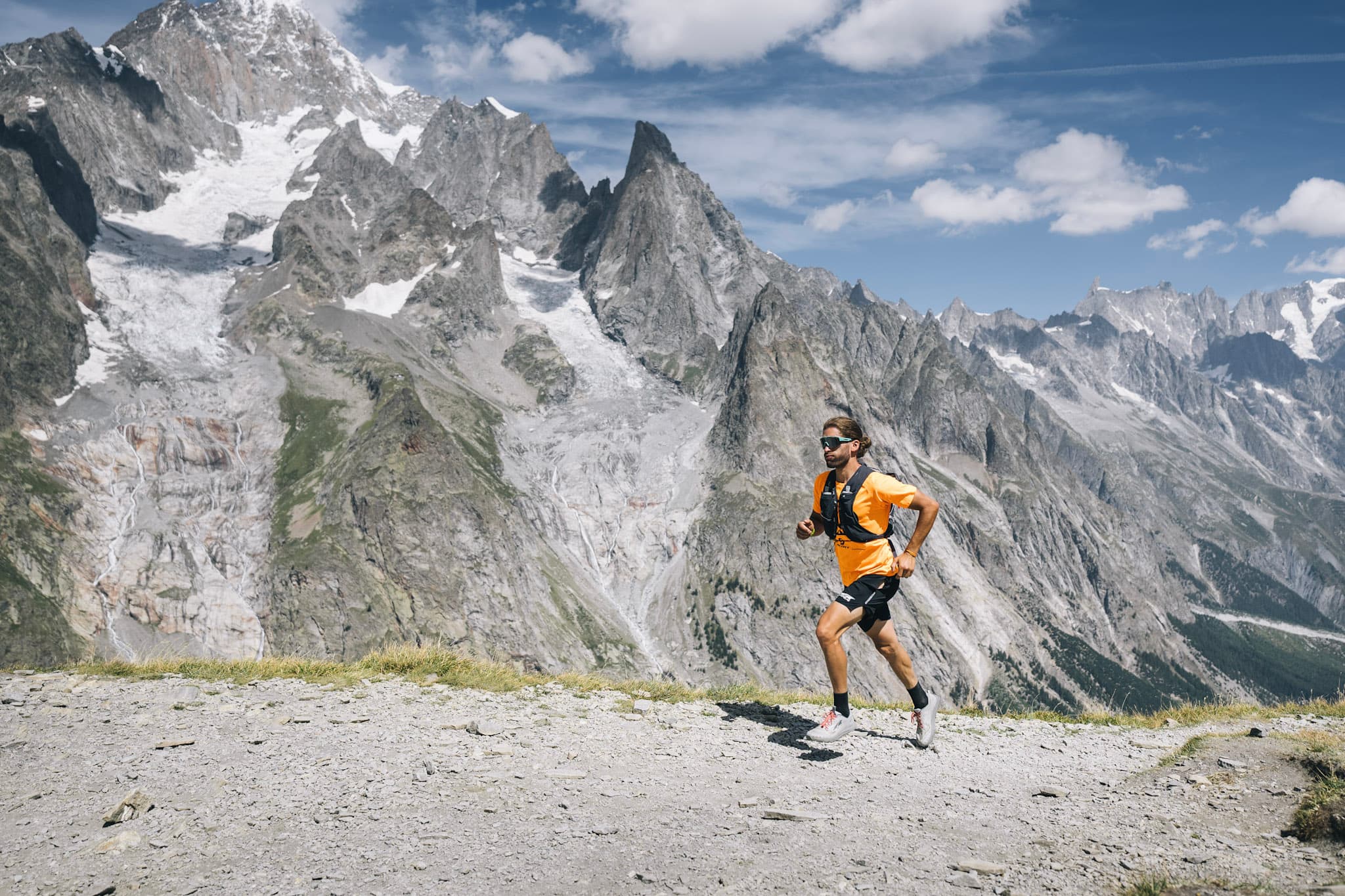 runner runs uphill on rocky trail with rocky alpine mountains in background