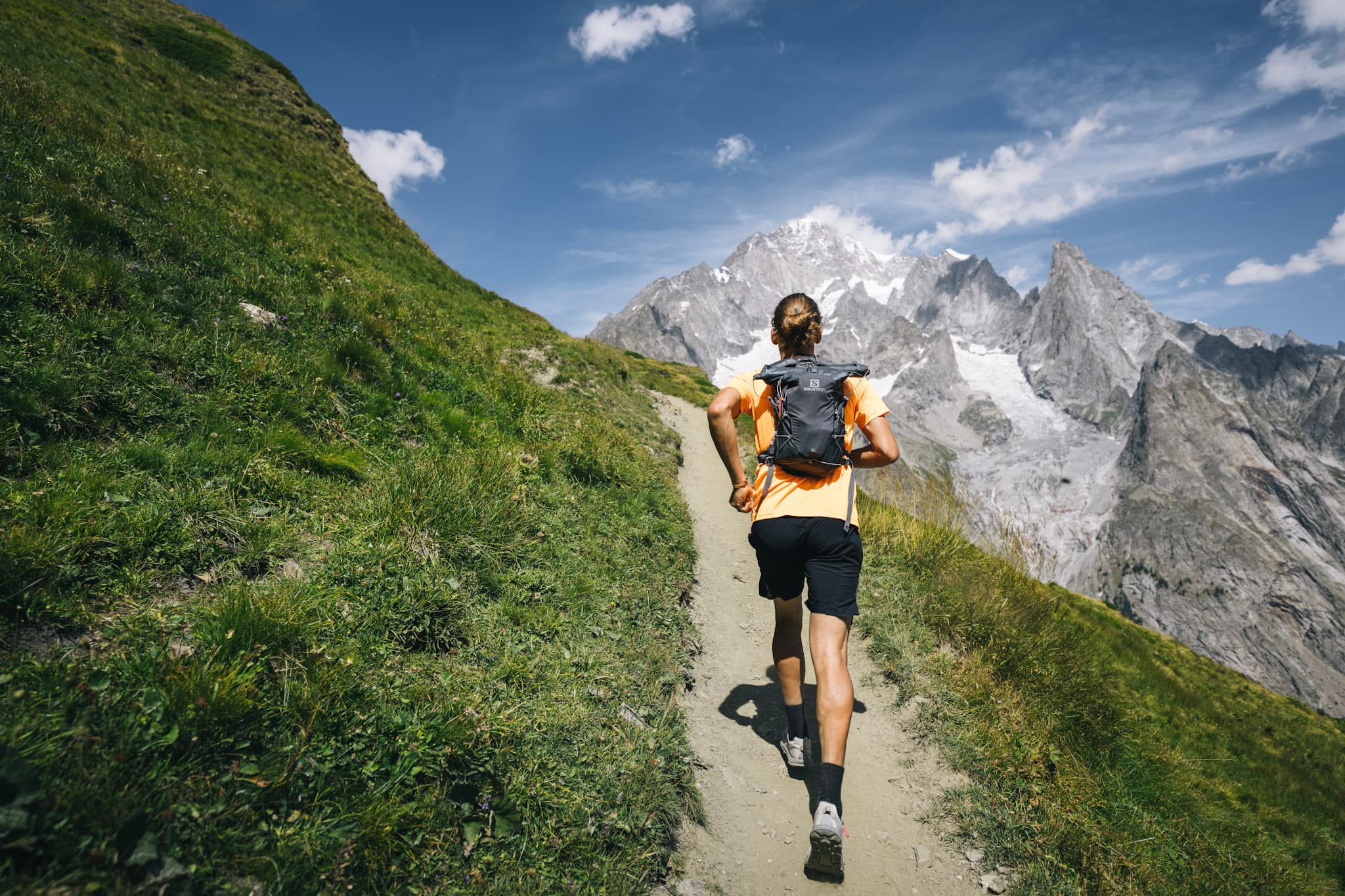 runner runs away from the camera towards big alpine mountains