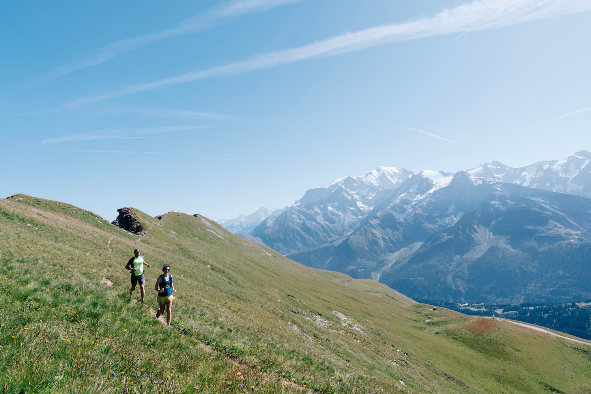 2 runners run down grassy trail with Mont Blanc massive in background