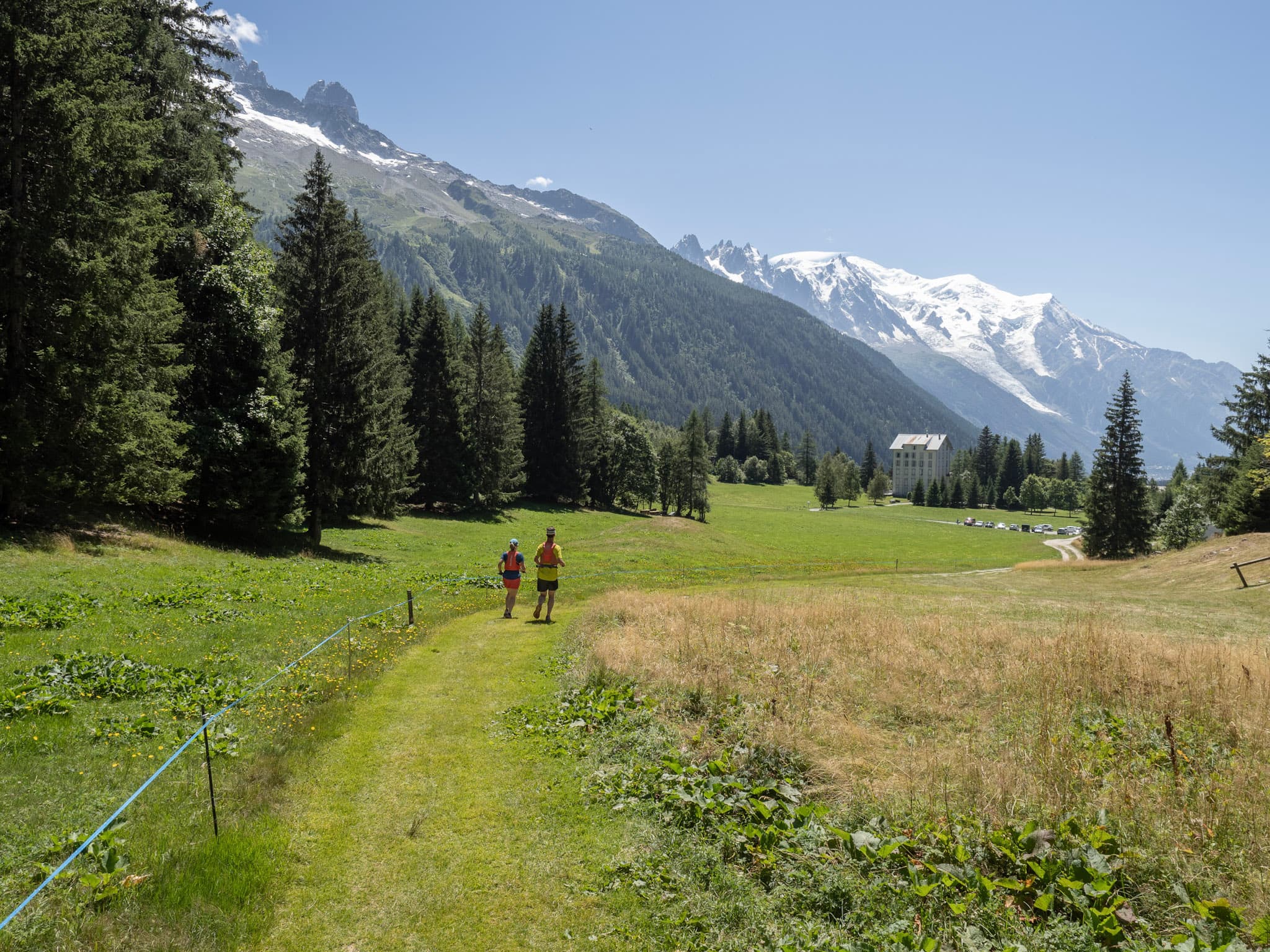 2 runners in distance in meadow with views down valley of Mont Blanc