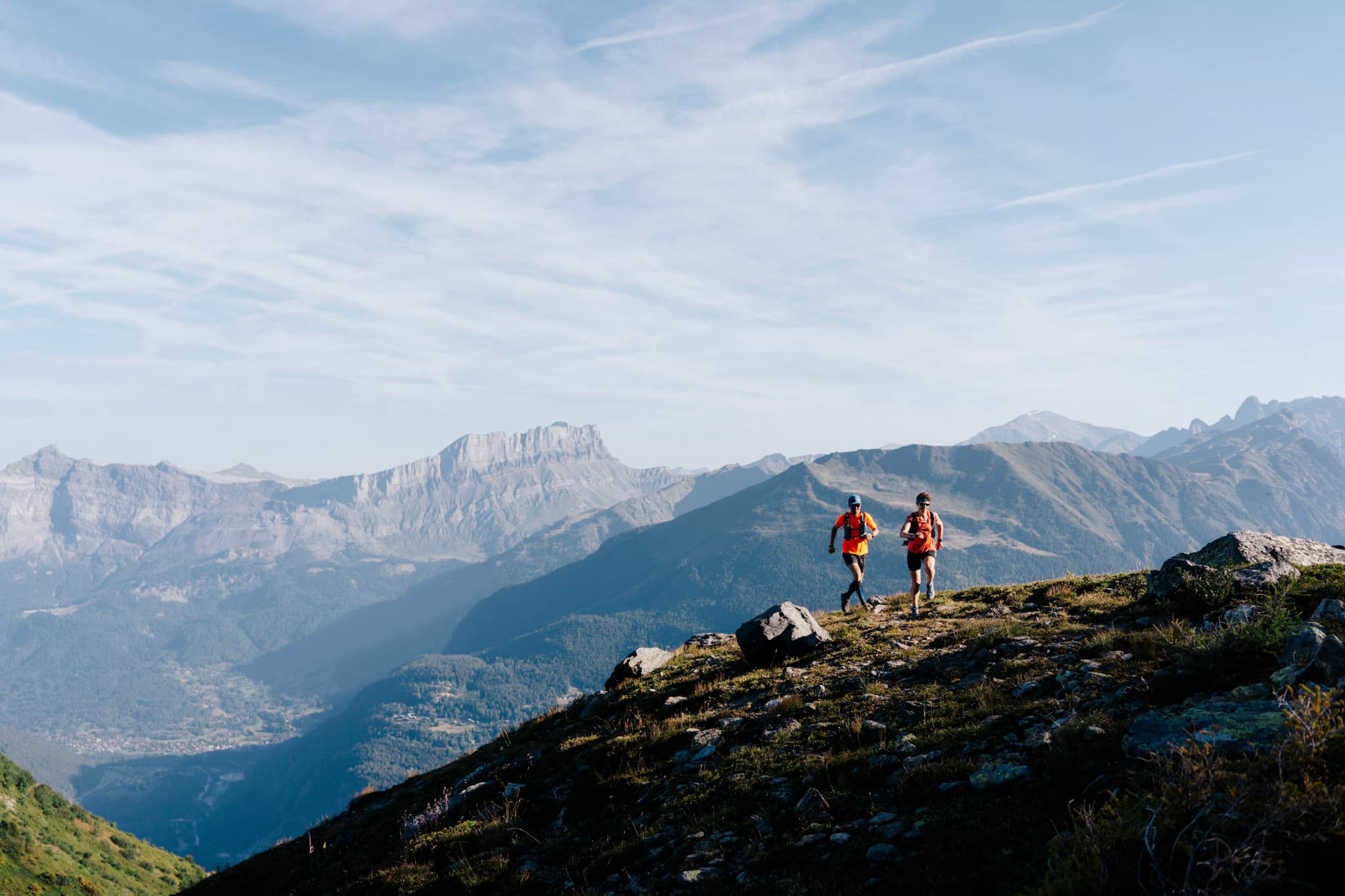 2 runners run up the trail with mountains in background