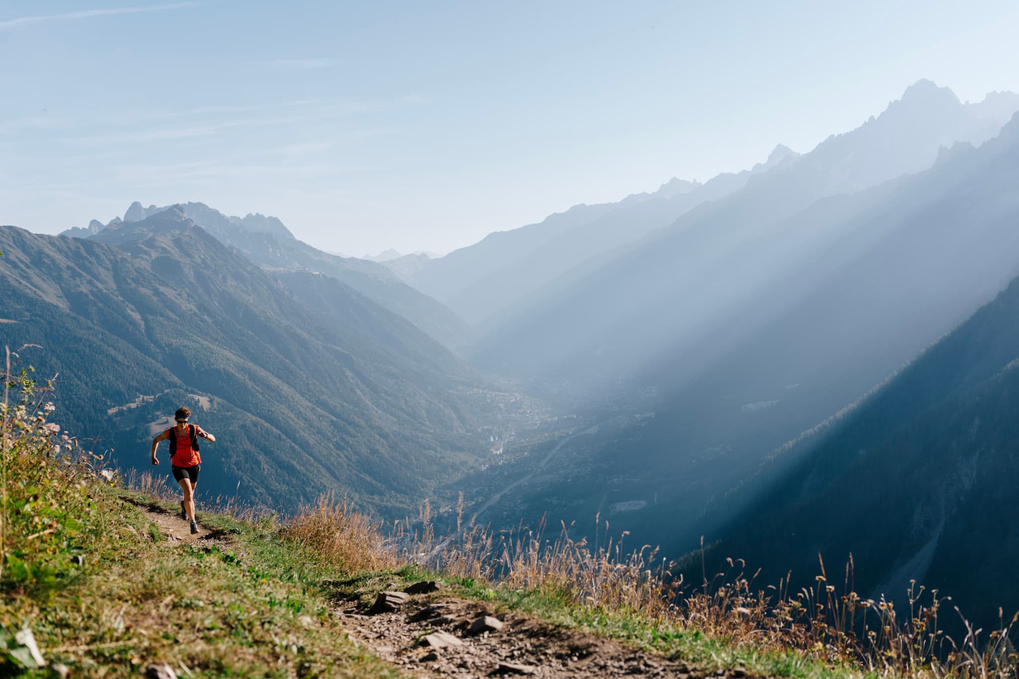 1 runner run up the trail with mountains in background. Morning light