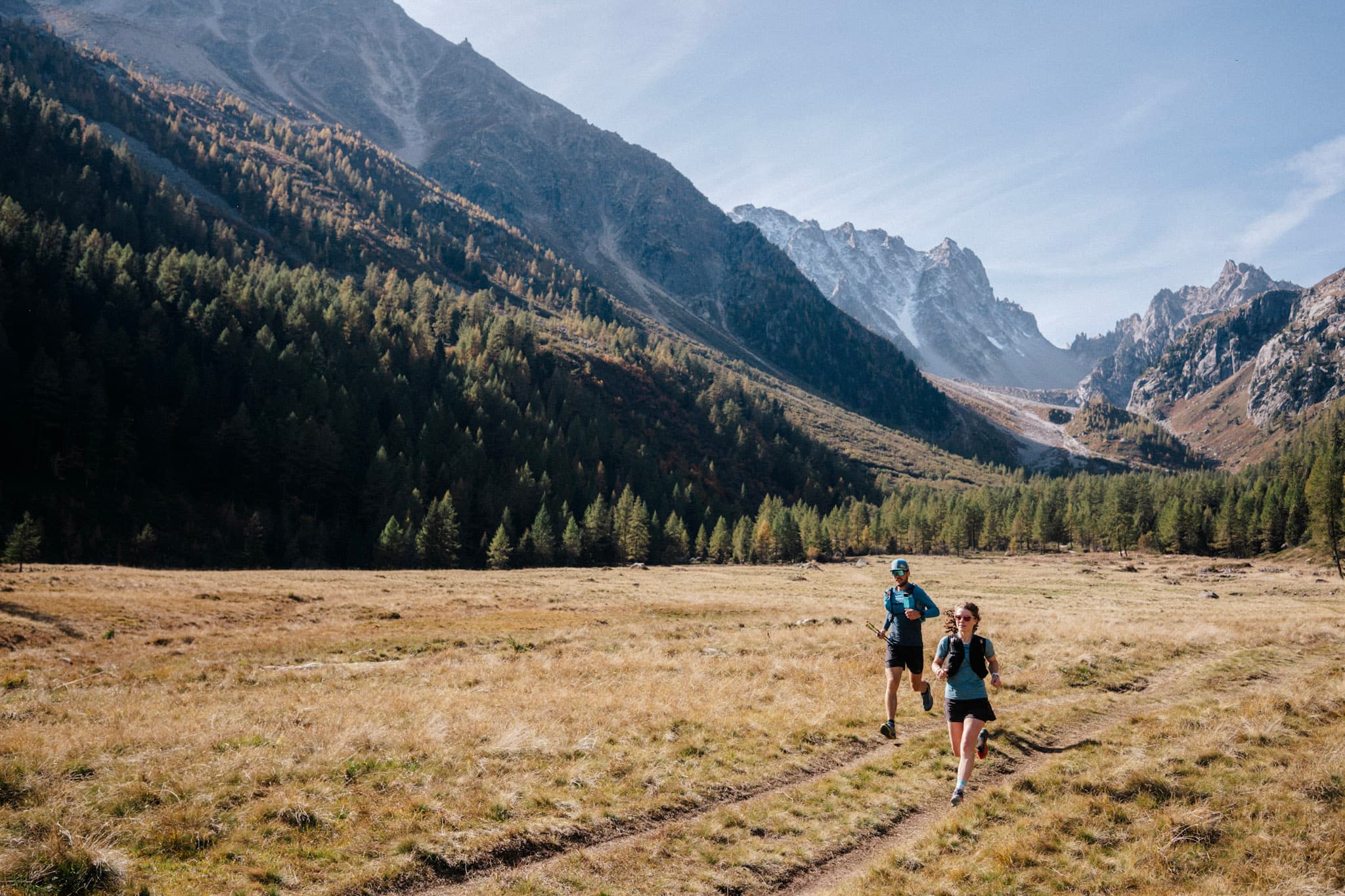 2 runners run alone flat meadow with mountains in background