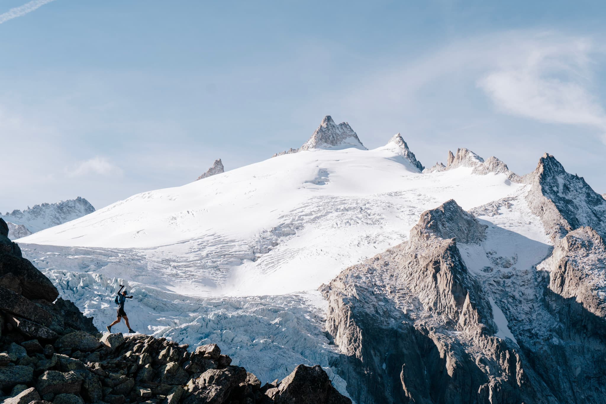 Runner in distance jumps between rocks with huge glacier behind