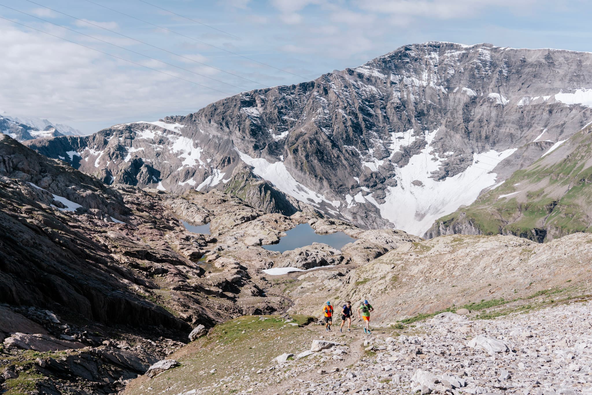 Three runners above Rocky Mountains, run, uphill Lake and snow behind