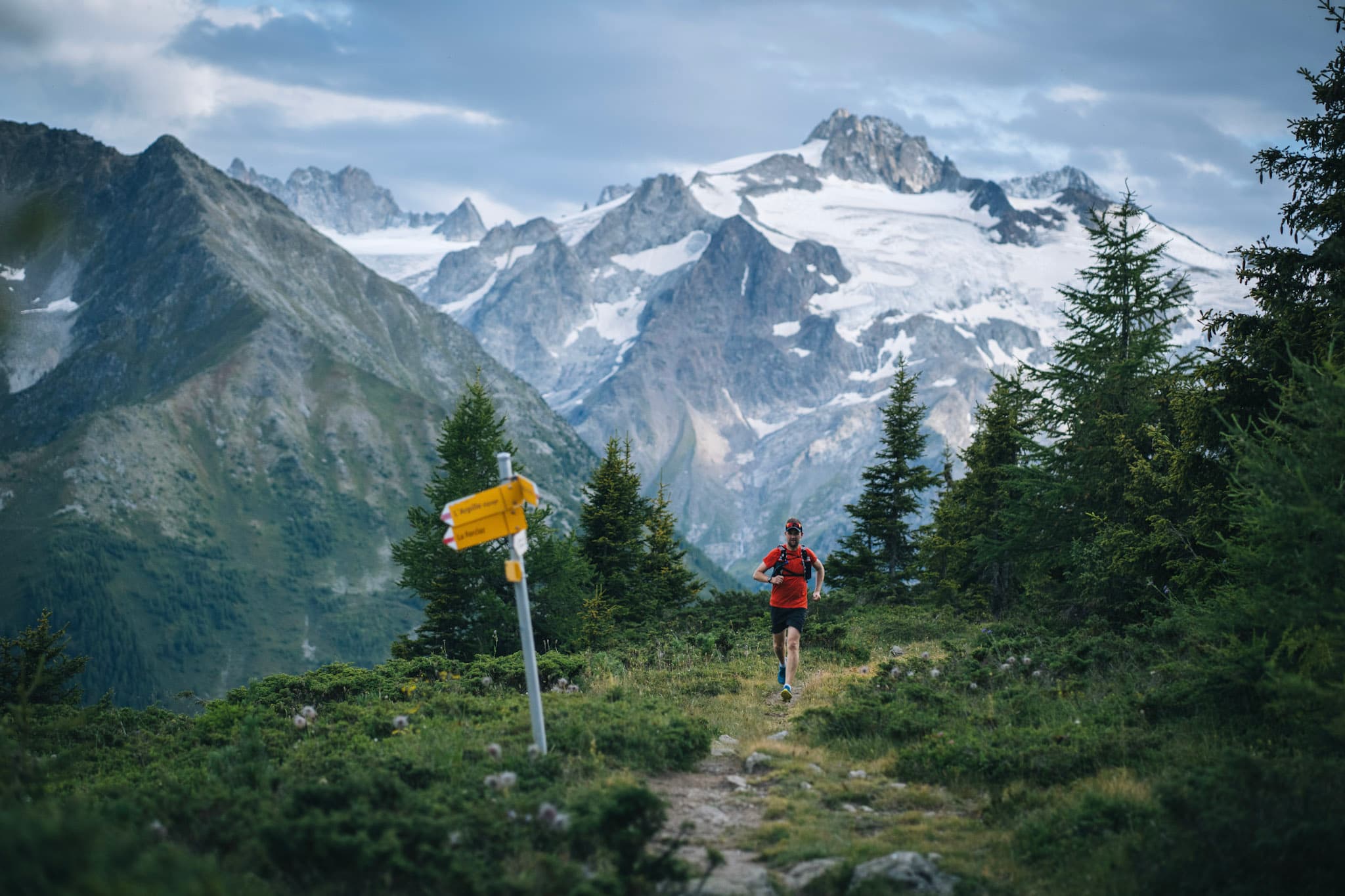 Runner running up hill with walking sign post in foreground and alpine mountains in background