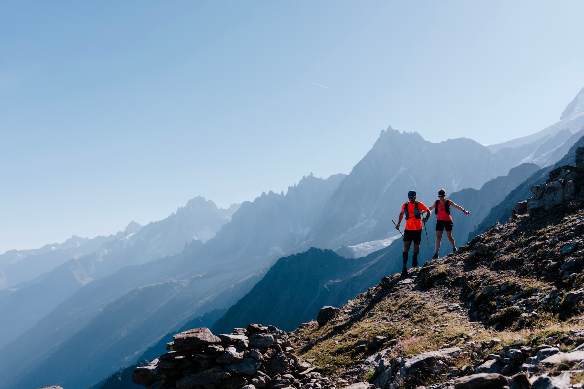 2 Runners run downhill with mountains in the background