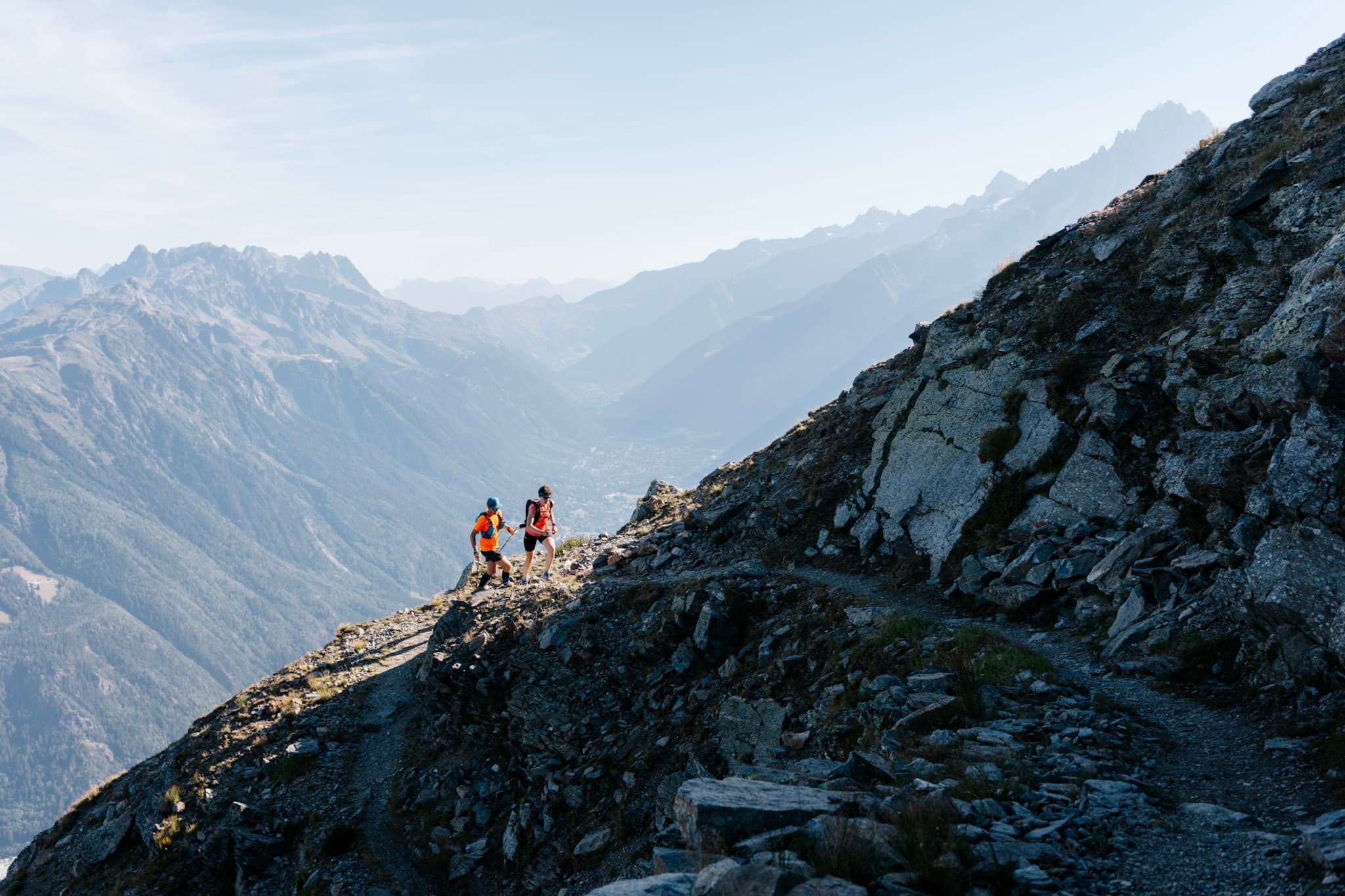 2 runners run up the trail with mountains in background