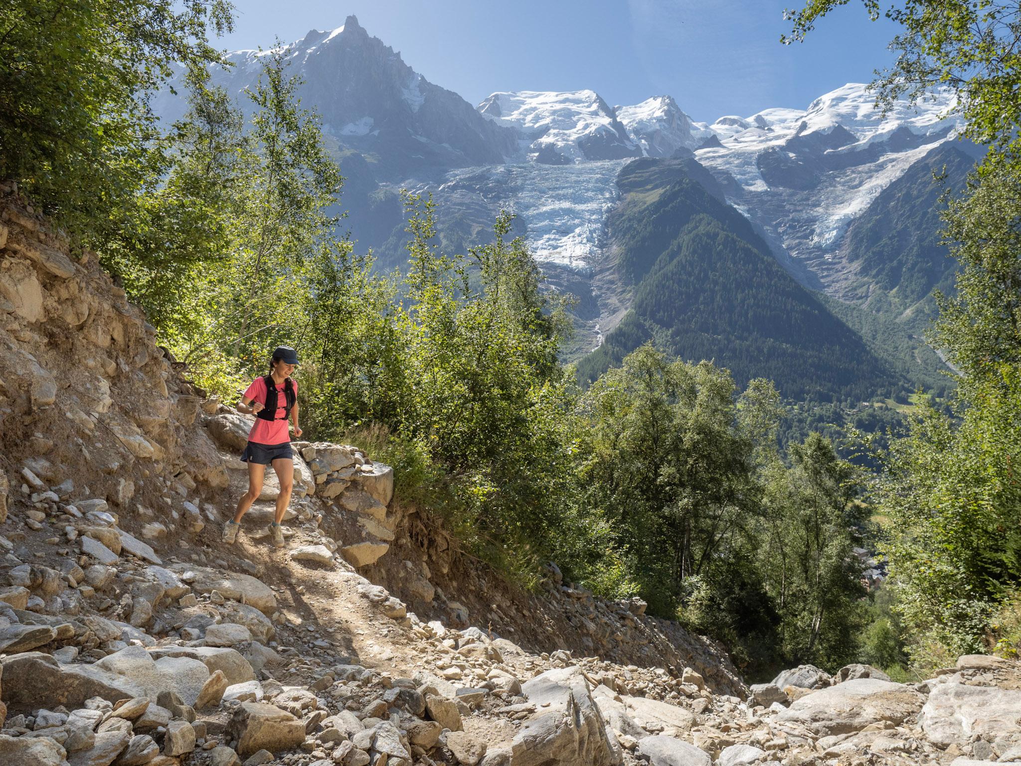 Runner running downhill on rocky trail in forest with view of alpine mountains