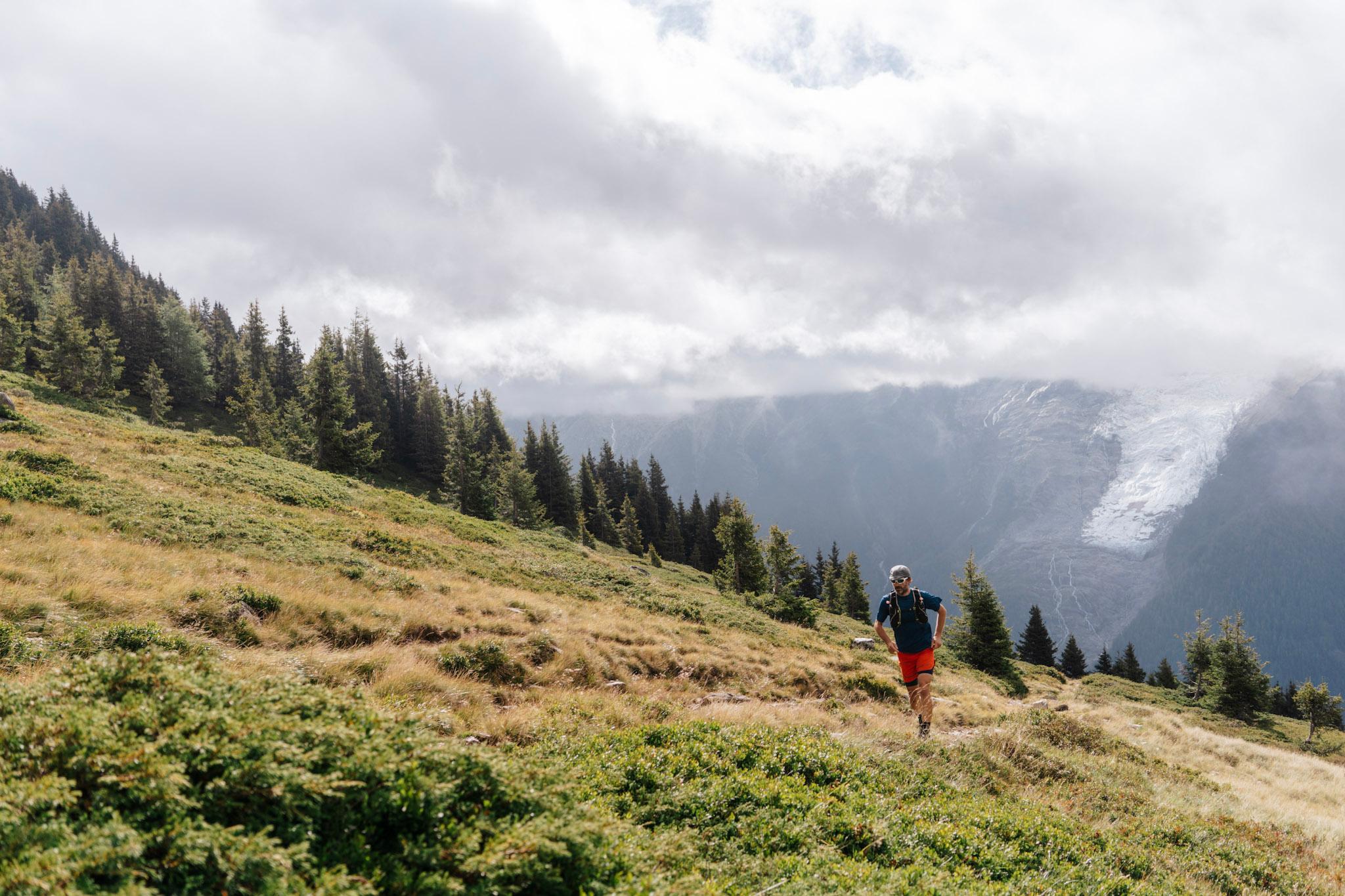 Runner runs uphill in Meadow with glacier behind