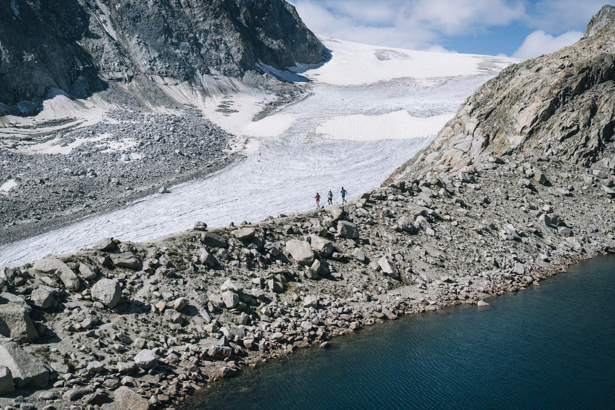 3 runners in distance silhouetted agains large glacier