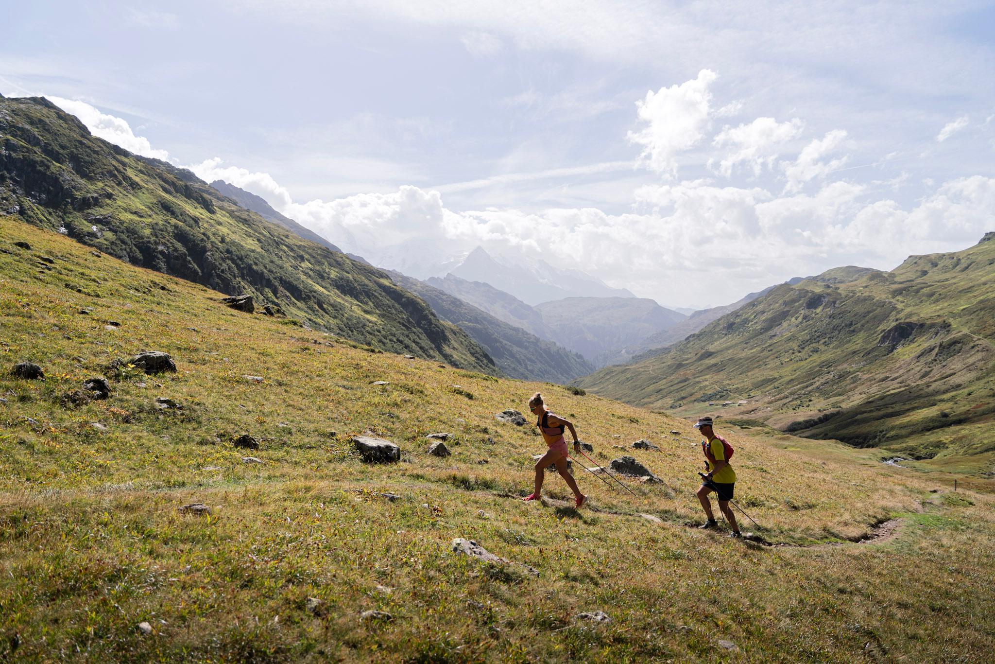 2 runners hike up hill towards col