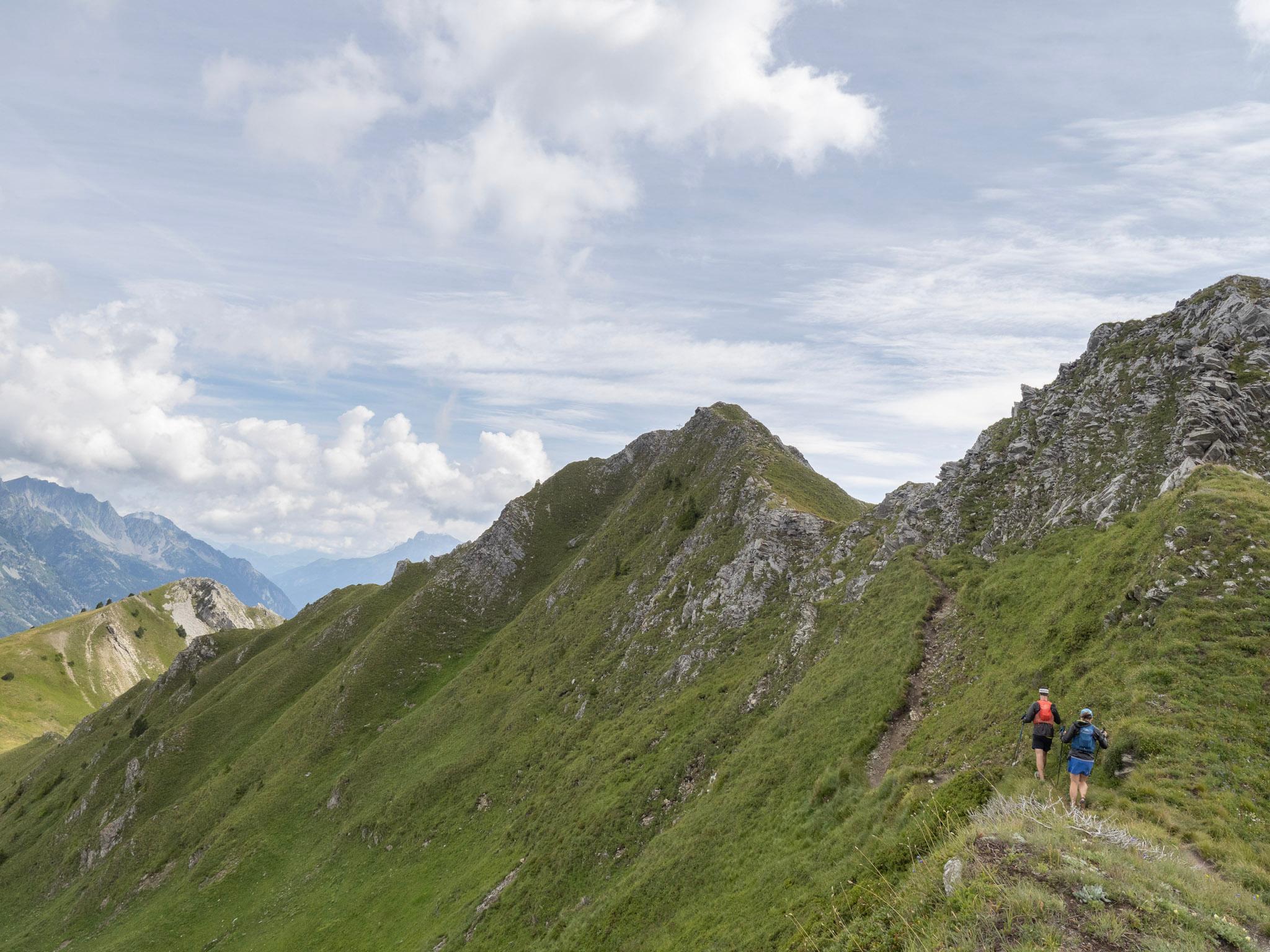 Runners traverse grassy trail next to ridge line