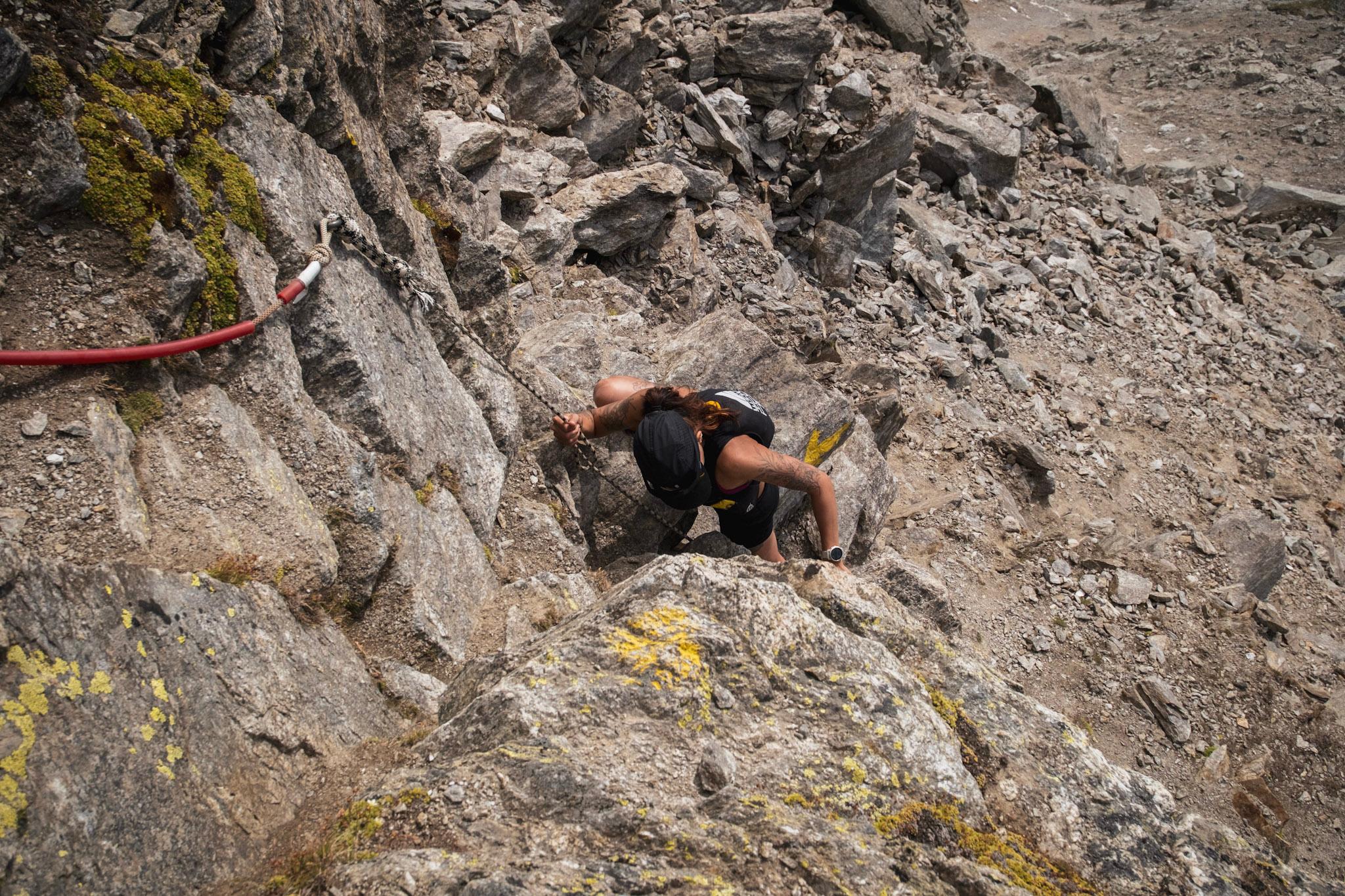 runner climbs up steep rocky ground using hand line for support