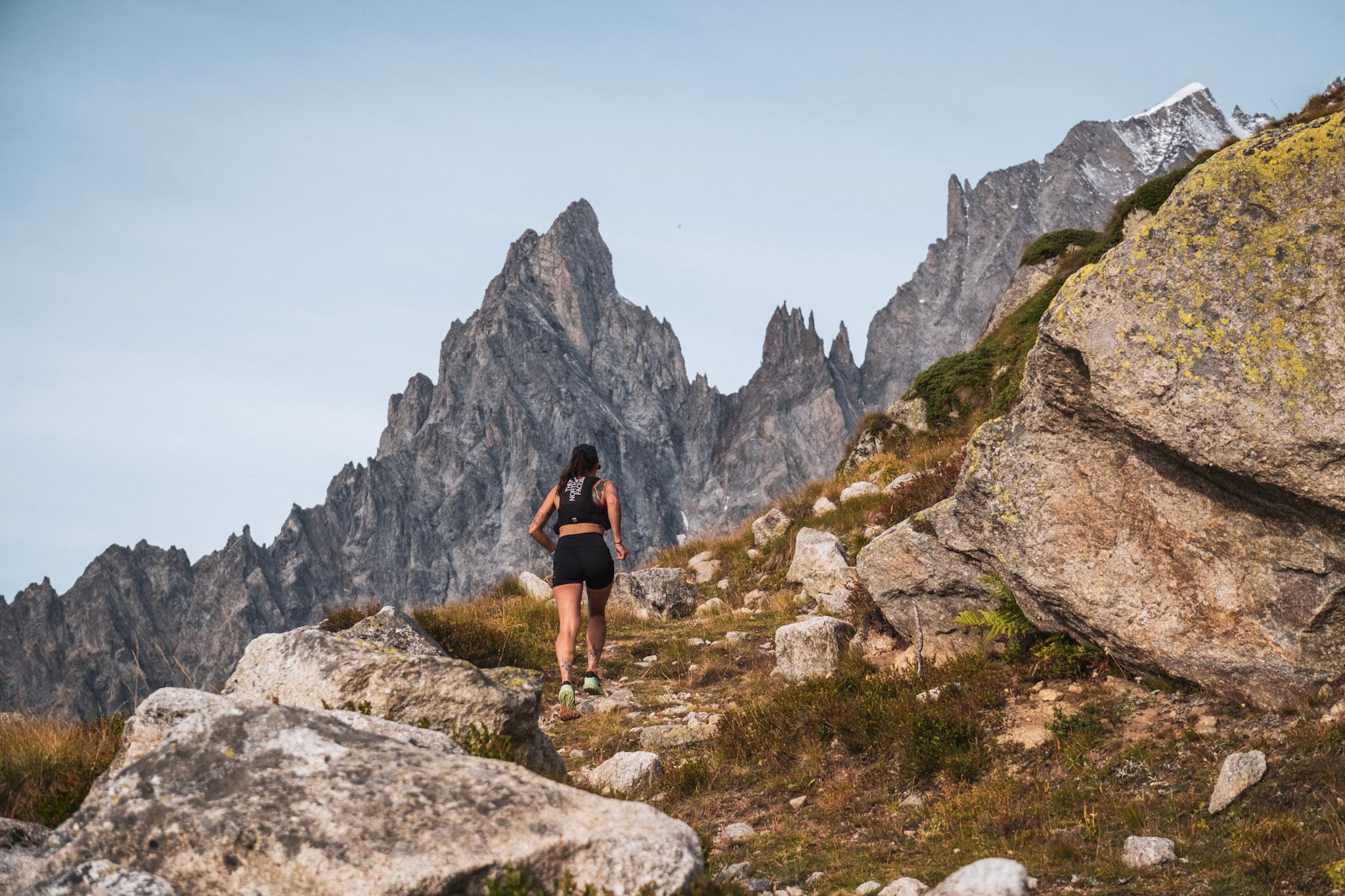 runner runs up hill with jagged Rocky Mountain spires in background