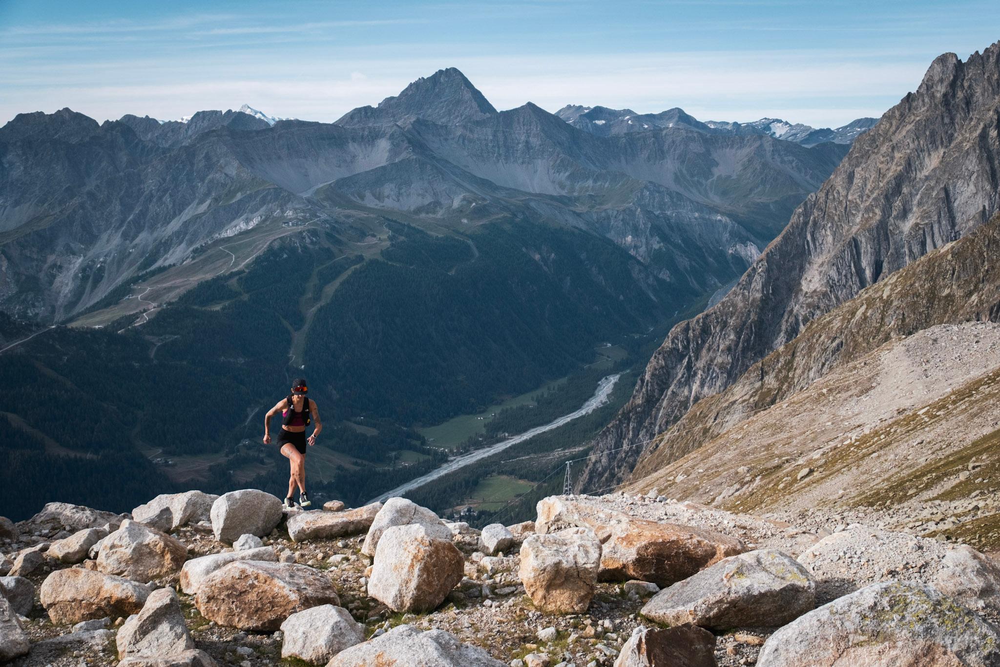 running runs up hill over rocks with green valley and Rocky Mountains in background