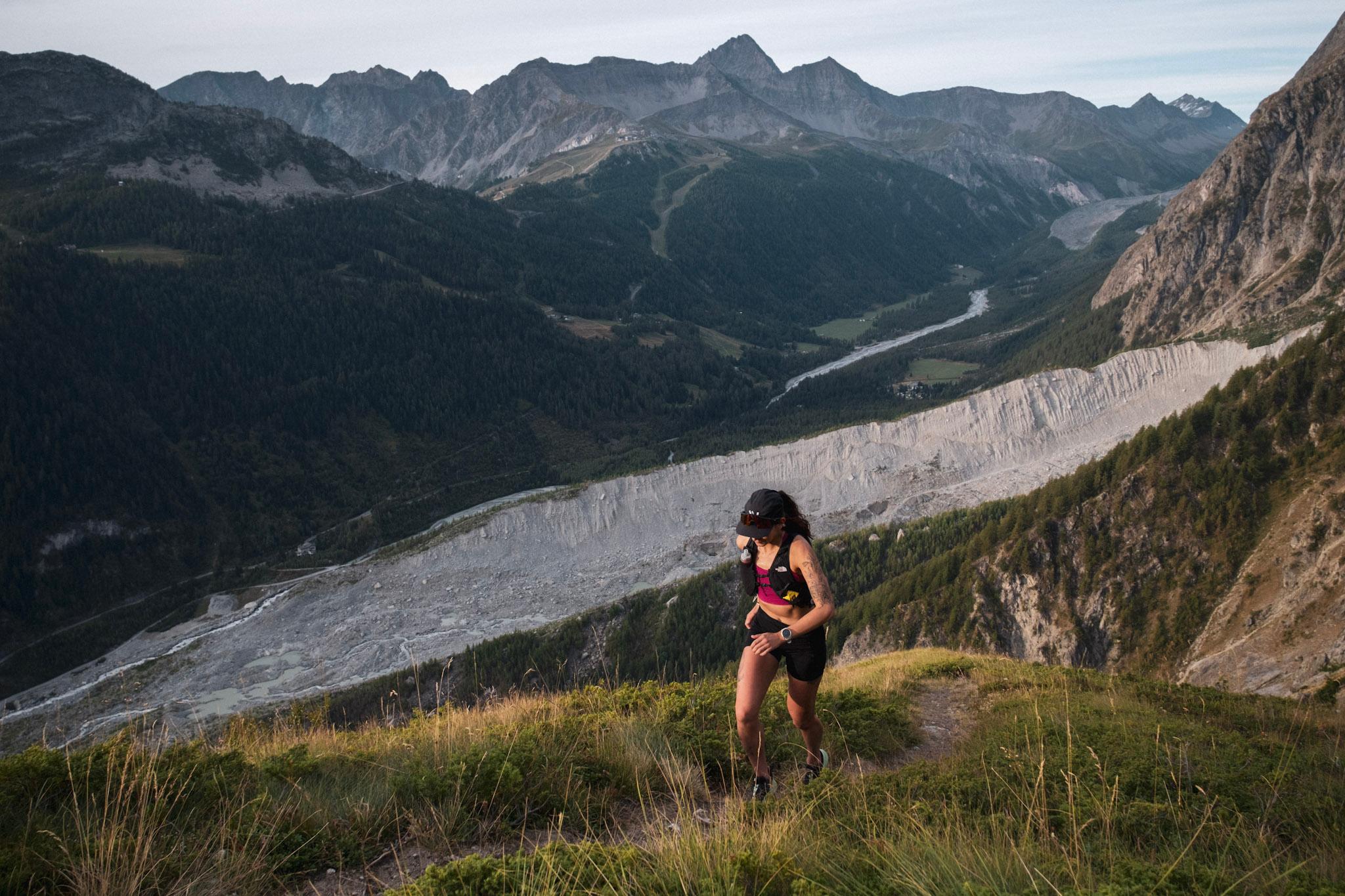 Runner hikes up hill in morning light with glacier in distance