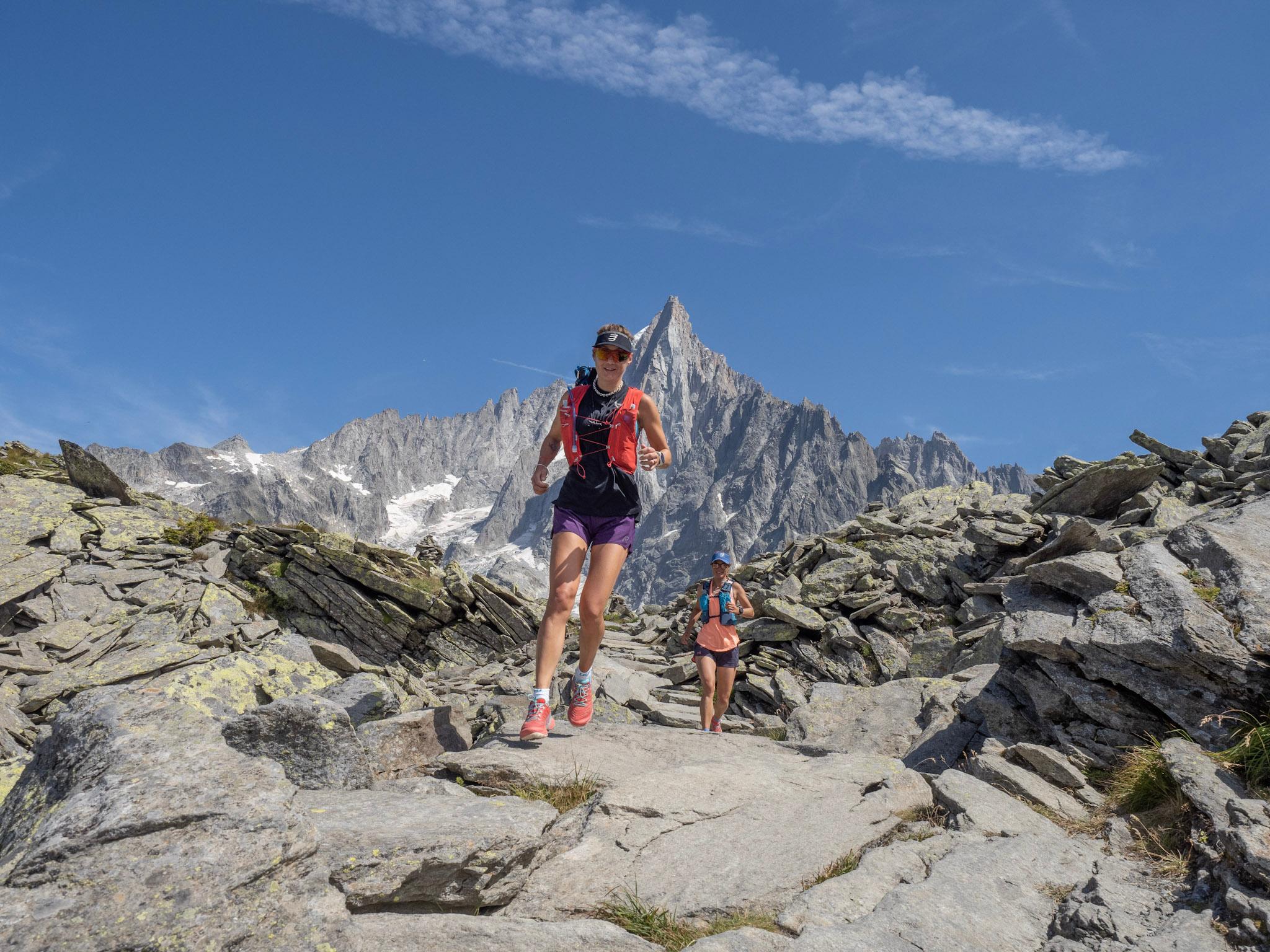 to runners run downhill on Rocky Trail, surrounded by boulders with Rocky mountain behind