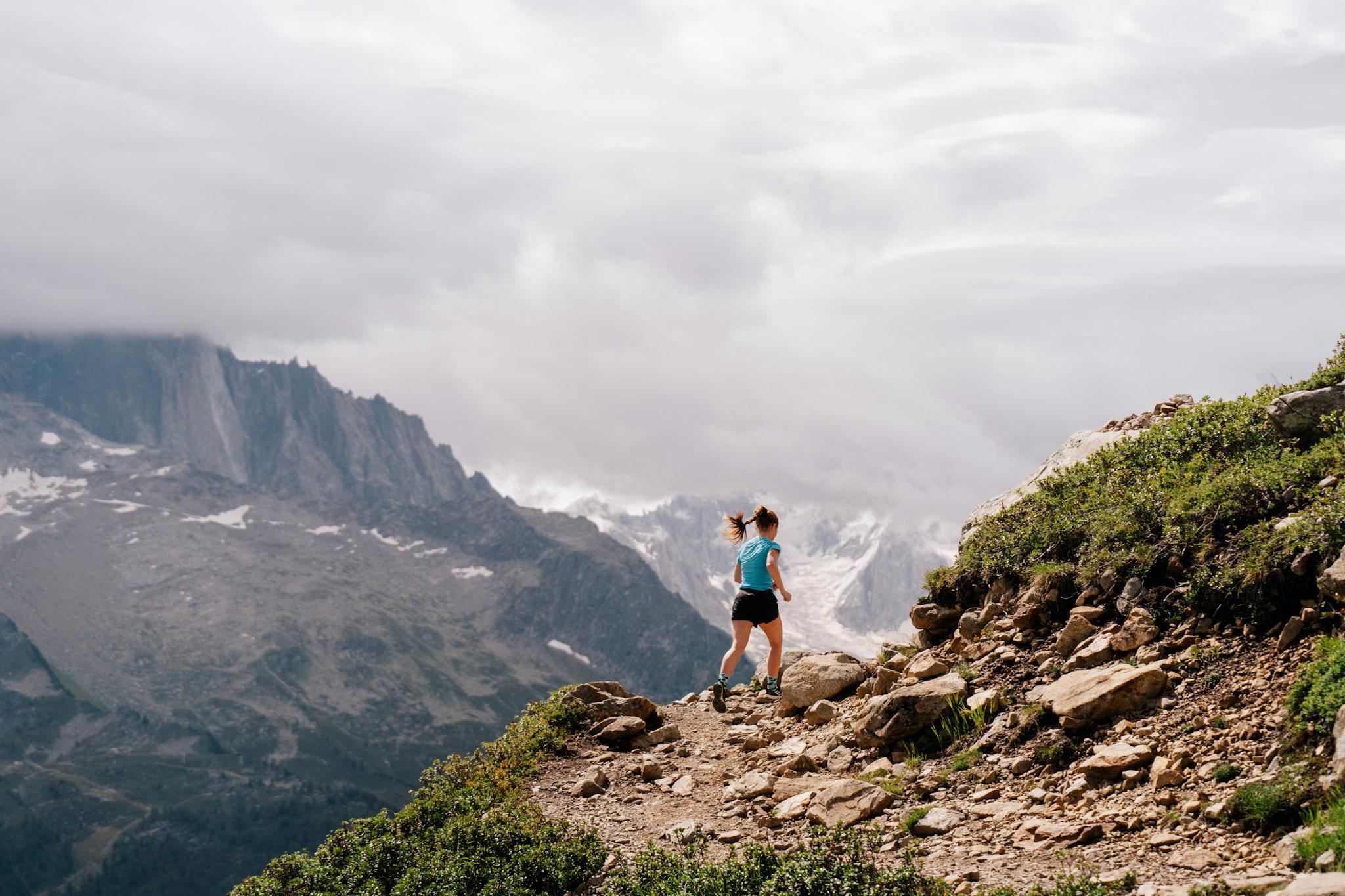 Runner runs up trail with cloudy mountains in the background