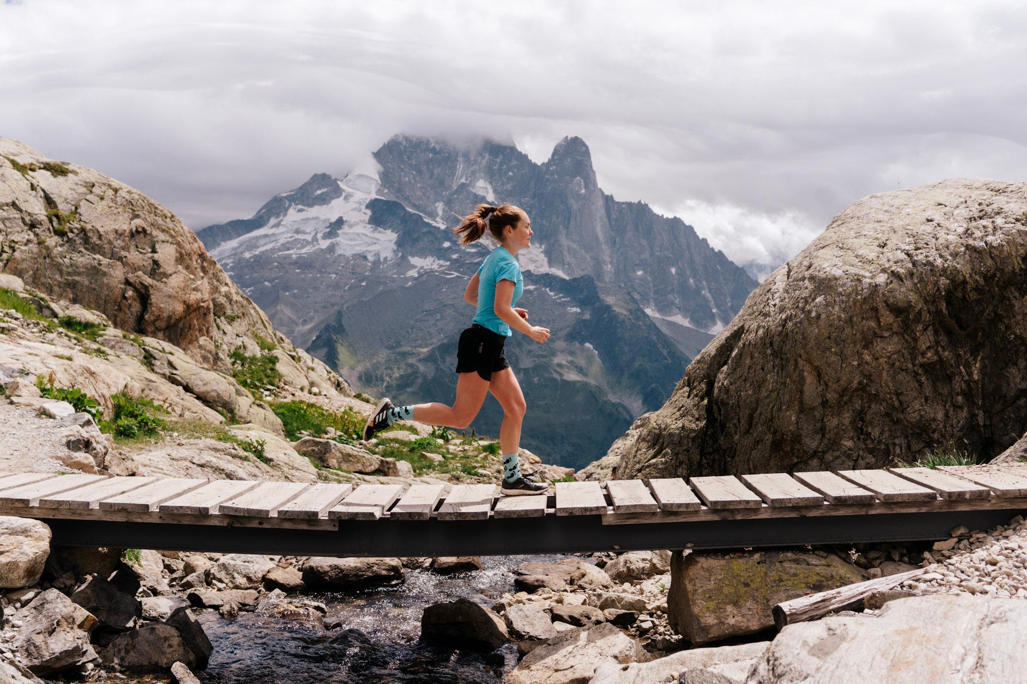 Runner runs across wooden bridge with Alpine mountains in the background