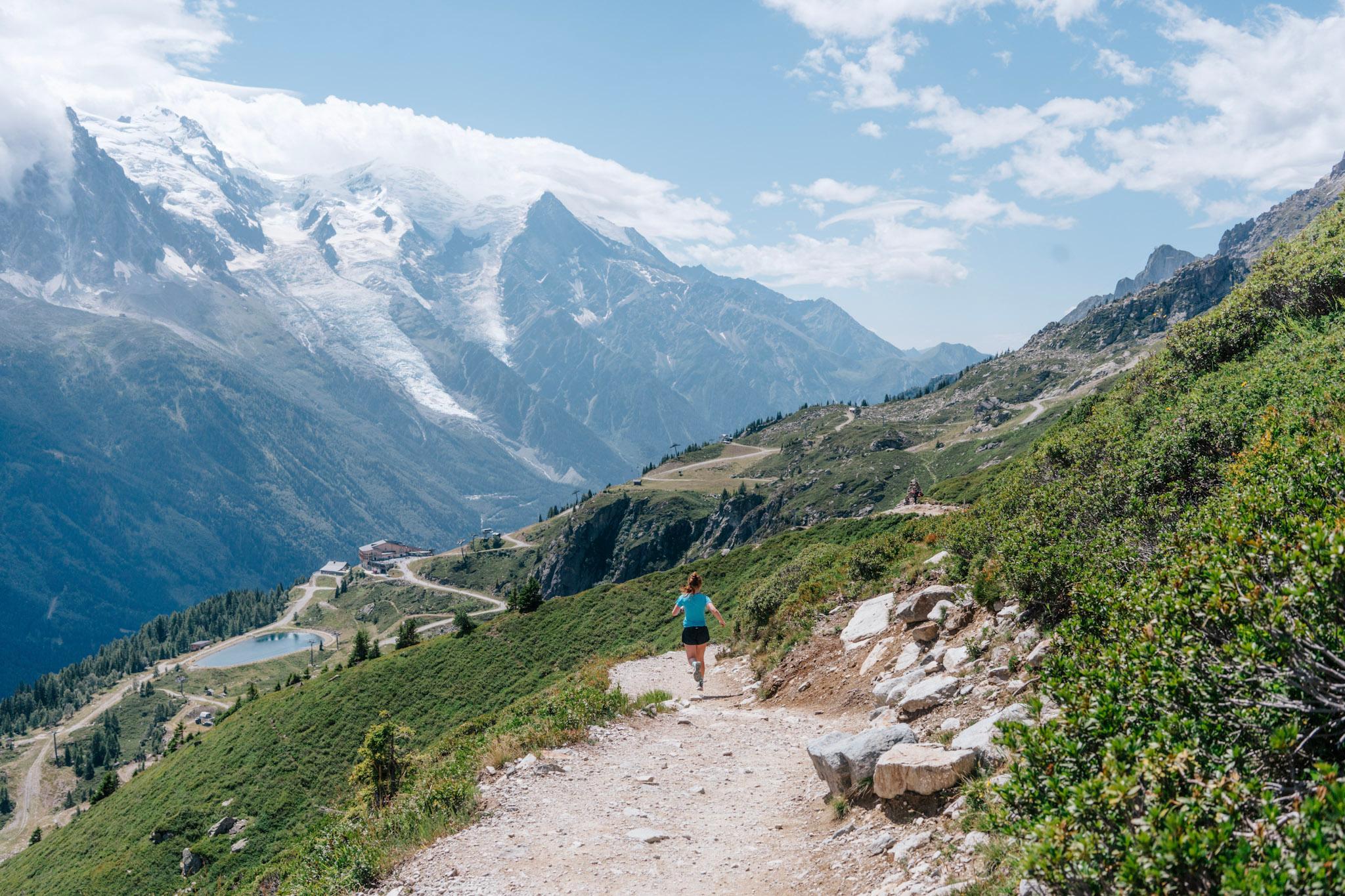 Runner runs downhill on Trail with Alpine Mountains in the background