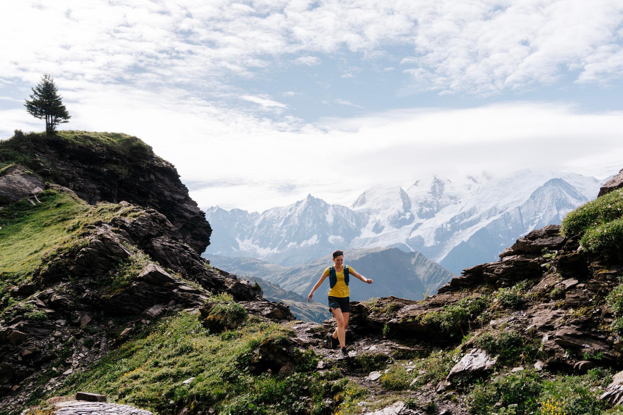 woman runs down trail with snowy mountains in the background