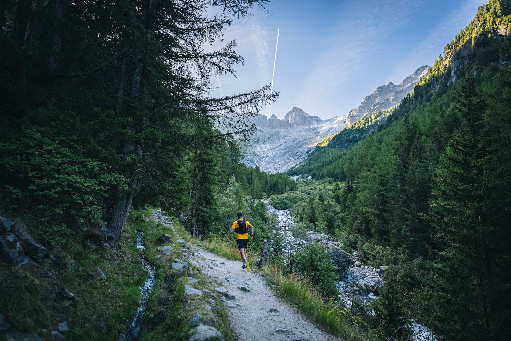 Runner running next to river in forest with alpine mountains above