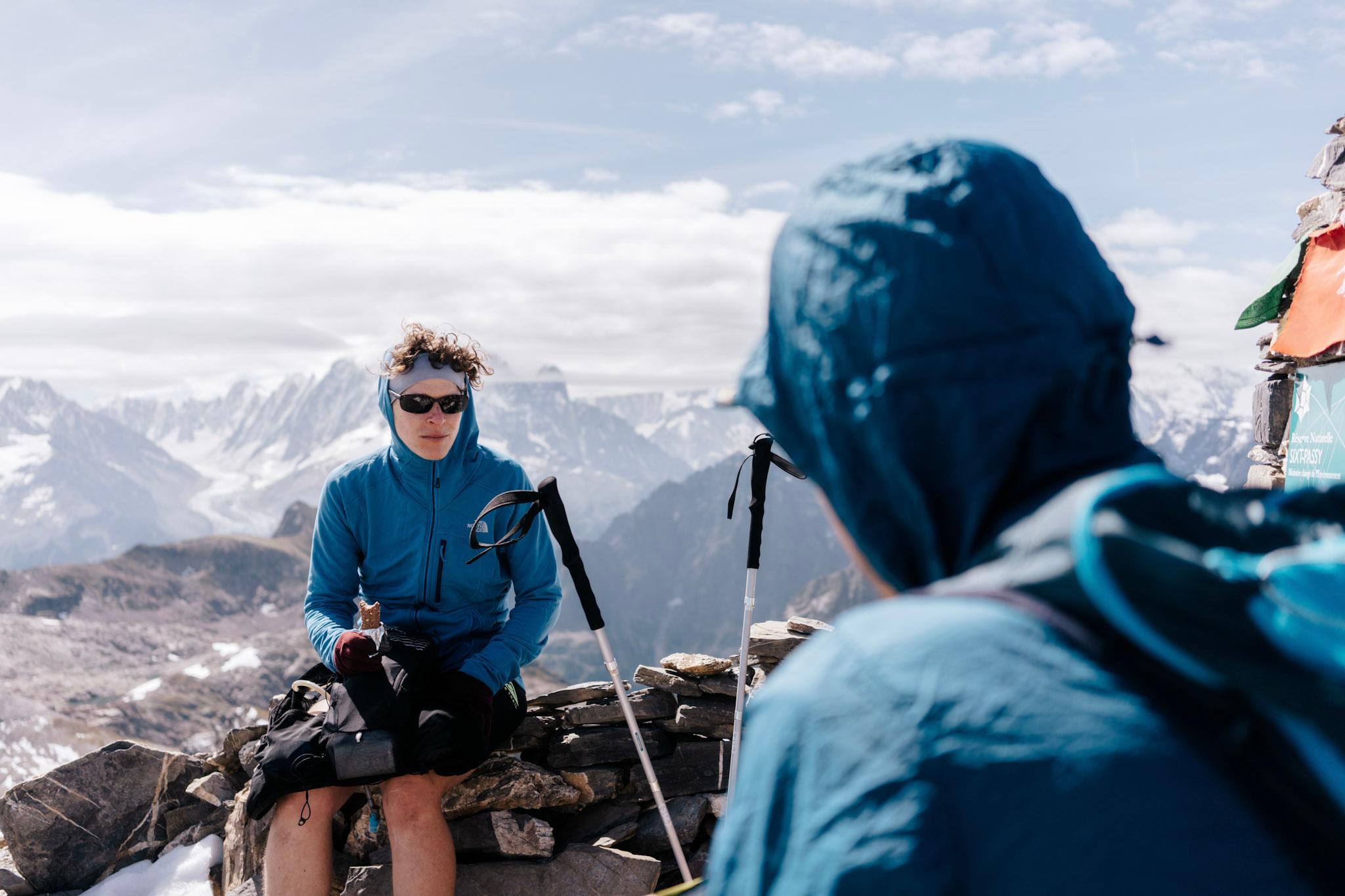 to runners sit on top of Rocky Summit with Alpine mountains in the background