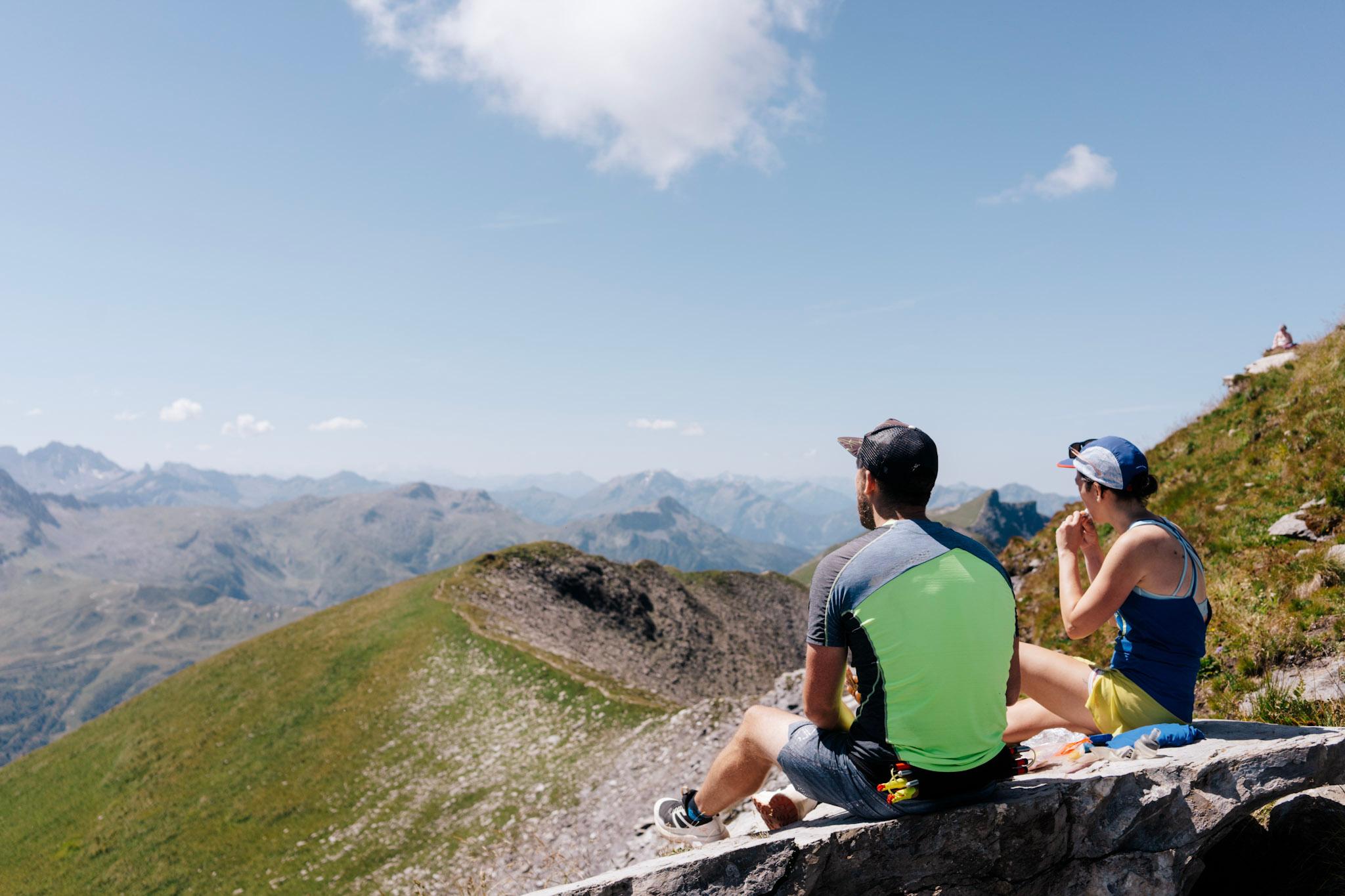 2 runners sit and look at the view from the summit