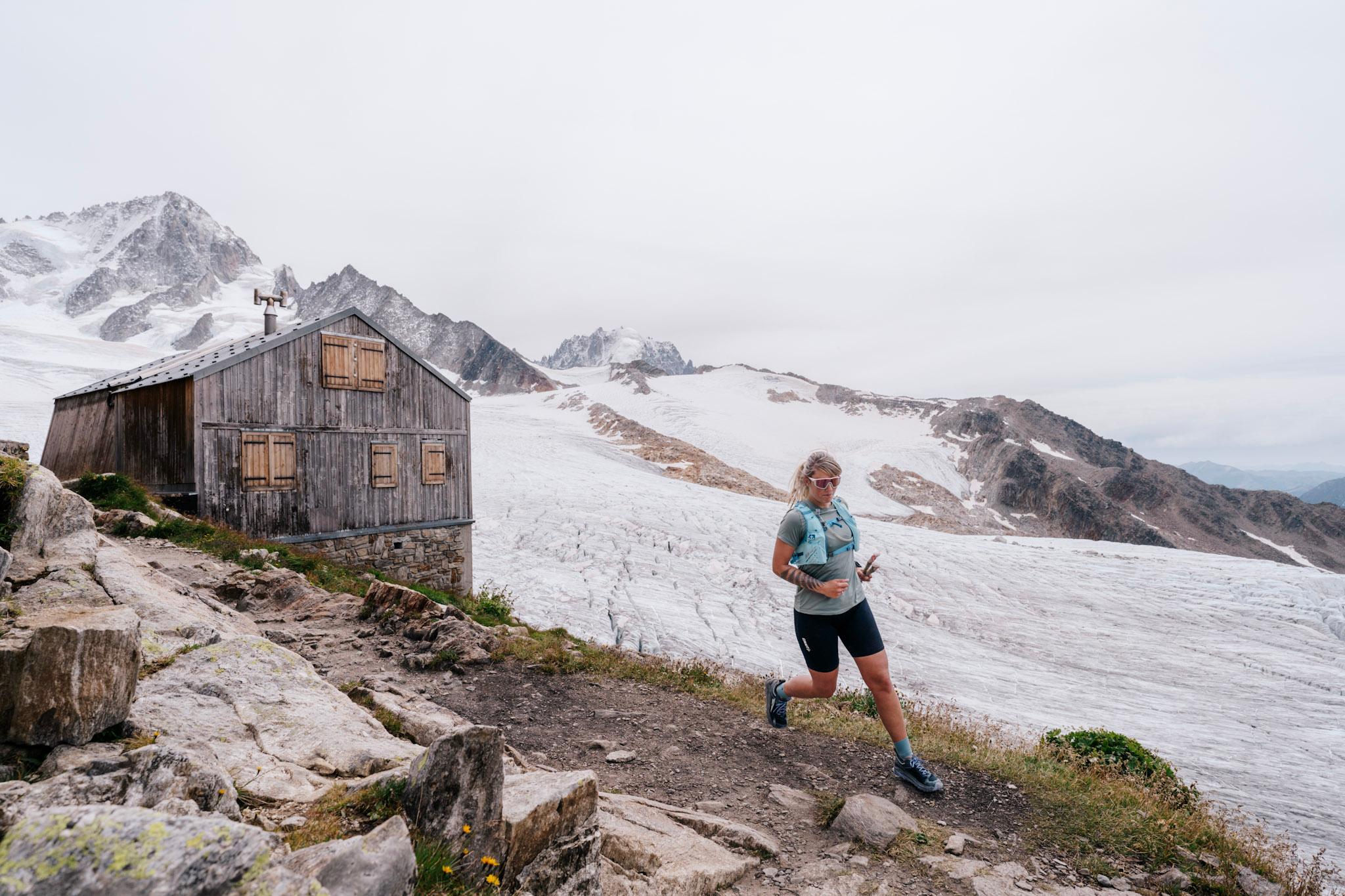 female runner runs next to mountain refuge and glacier