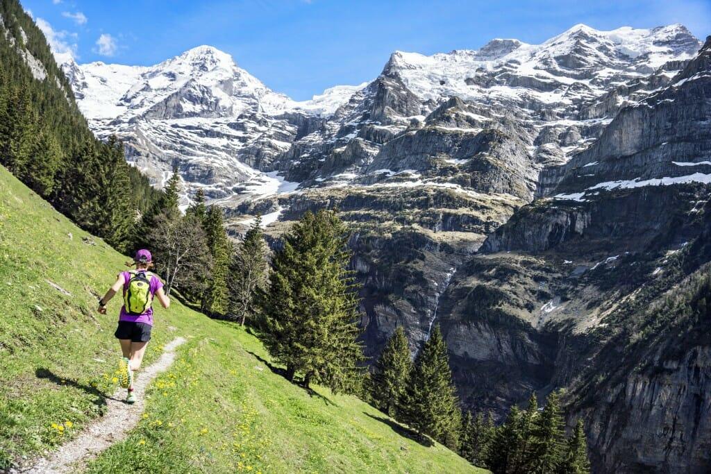 One woman trail running on the Trummelbach Falls Trail from Lauterbrunnen to Wengen, Switzerland, with views of the Jungfrau above.