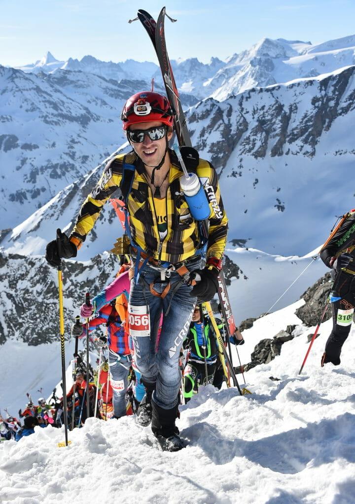 Sam Hill with skis on his backpack during a skimo race with lots of athletes behind himkimo