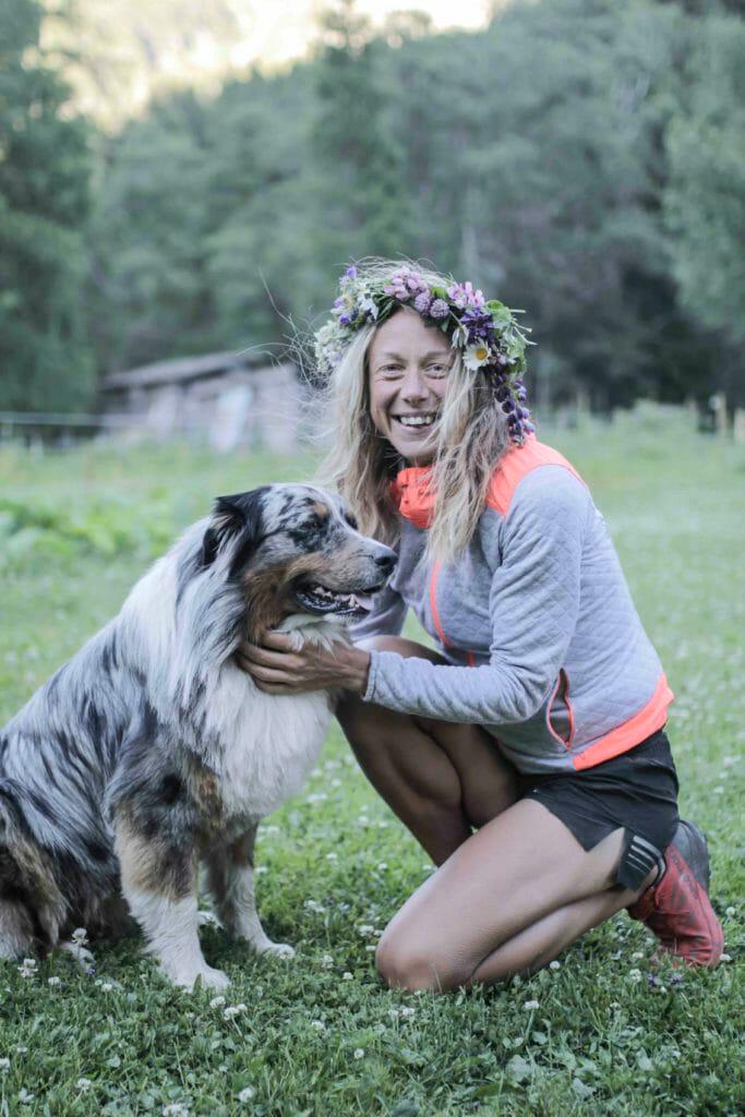 Mimmi Kotka with a flower wreath around her head, kneeled down with her dog