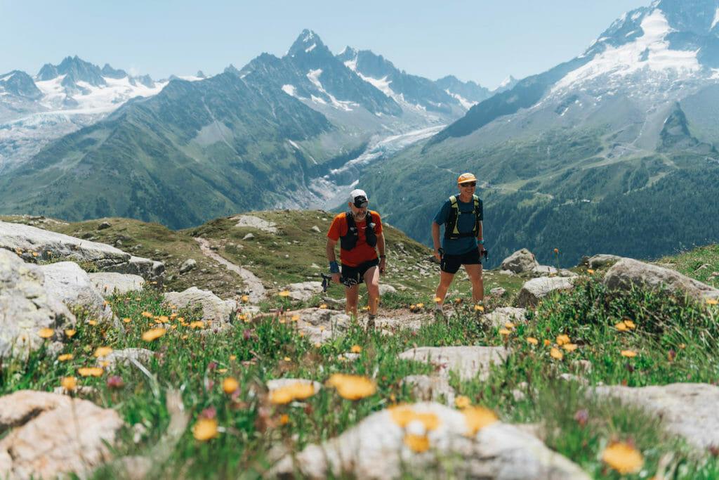 Two trail runners walking uphill through meadows in the Chamonix valley