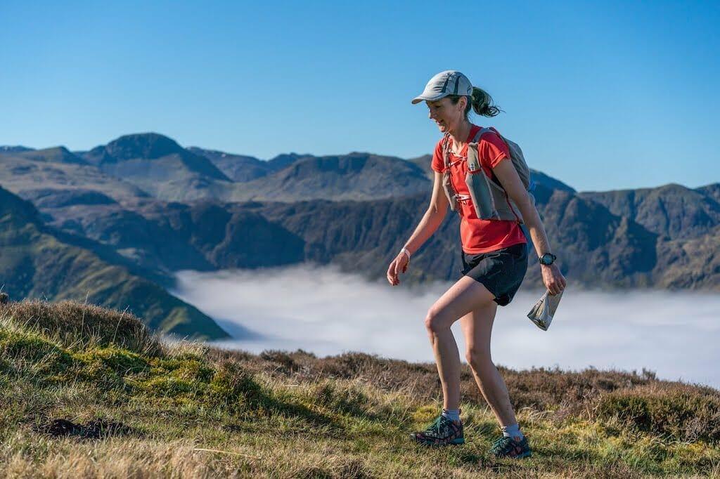 Heather Ohly walking on grass with a map in her hand above the clouds, in the Lake District