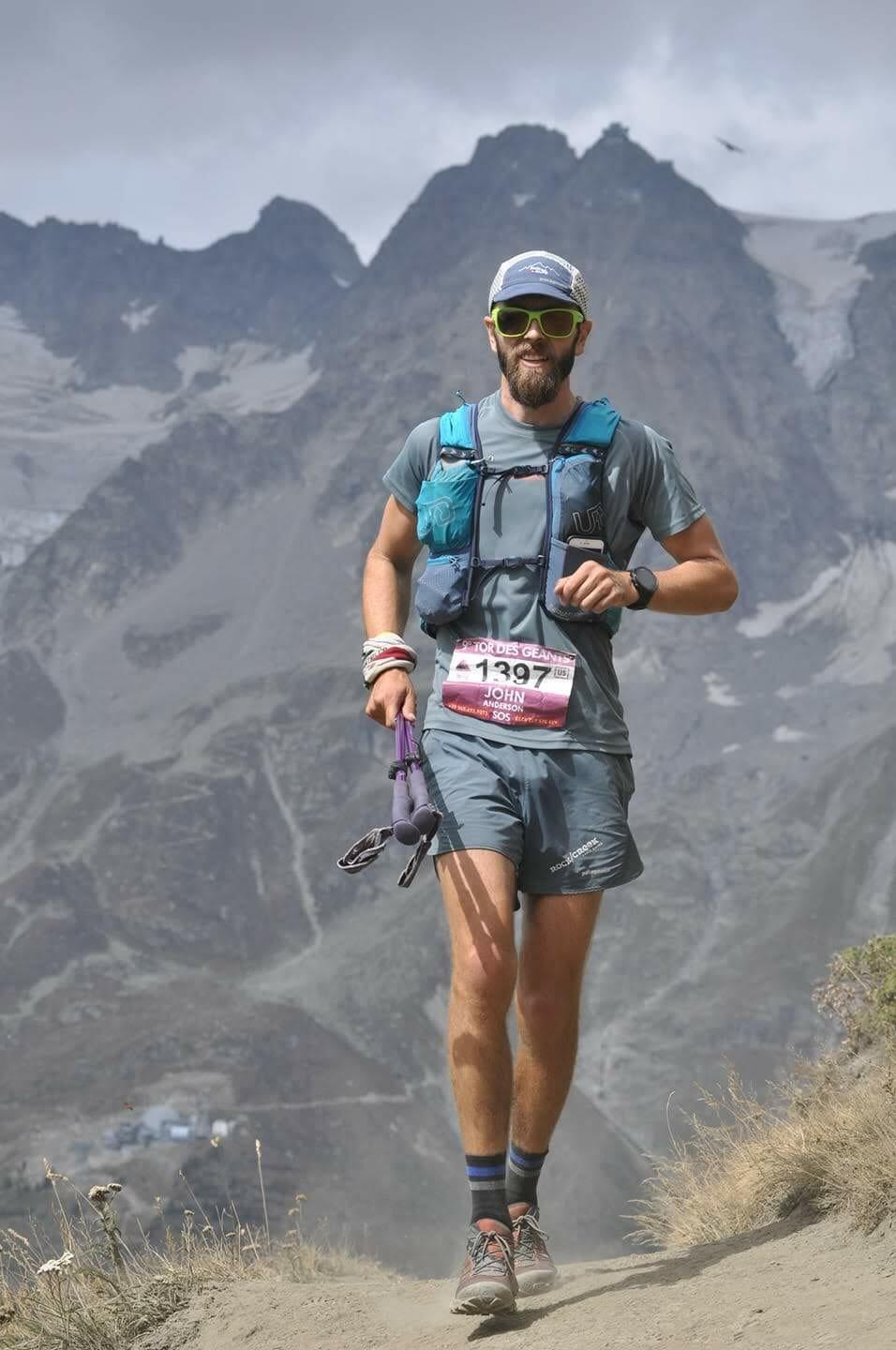 Trailrunner with grey shorts and shirt and 2 poles in his right hand