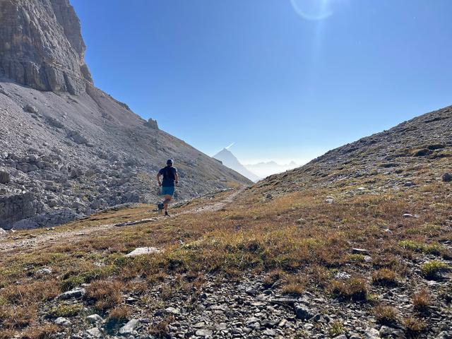 A trail runner running up a grassy hill in the Dolomites