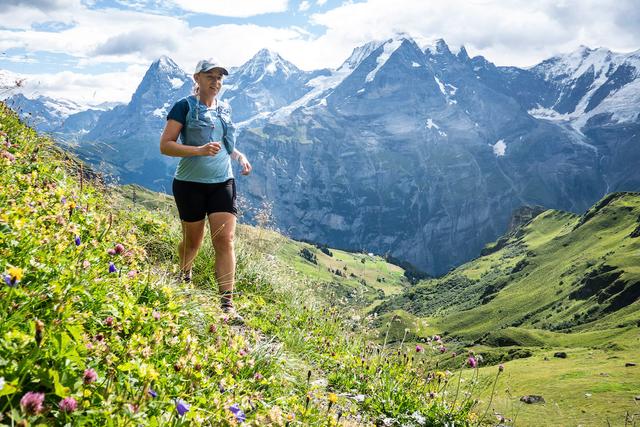 A female trail runner on a flowery trail with a mountain backdrop in the Bernese Oberland